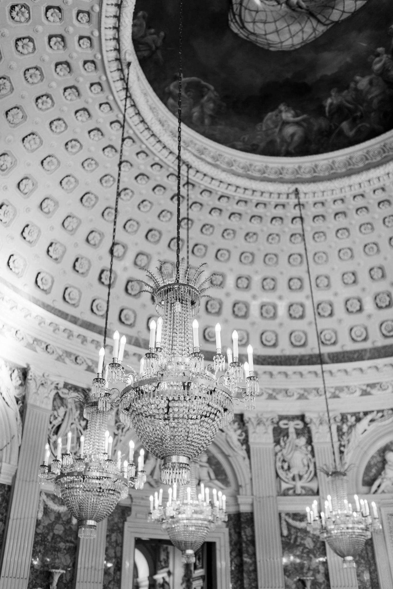 An ornate crystal chandelier hangs from a decorated dome ceiling in black and white.