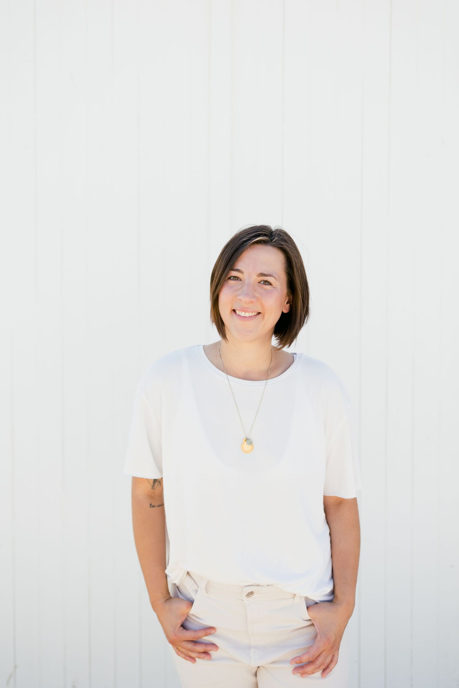 Professional in casual white attire standing against a white wall with a bright smile.