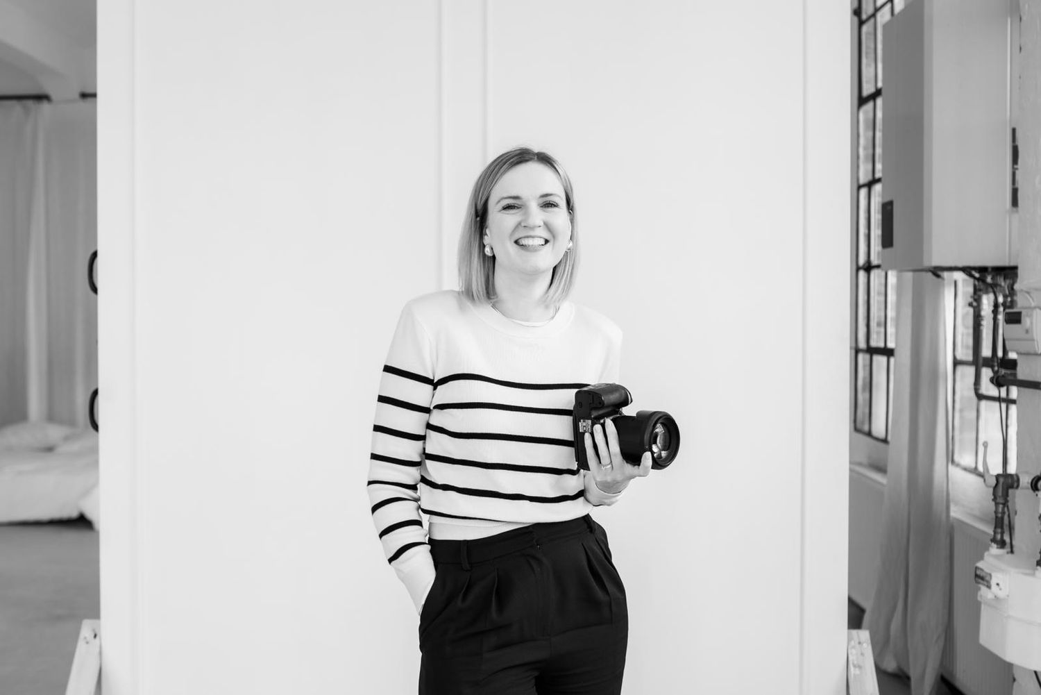 Black and white portrait of woman in striped sweater holding camera and laughing.