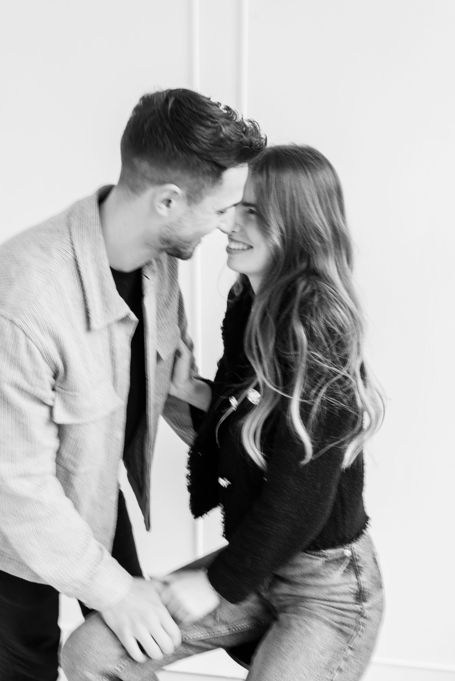 Black and white romantic portrait of couple embracing and smiling intimately against white wall.