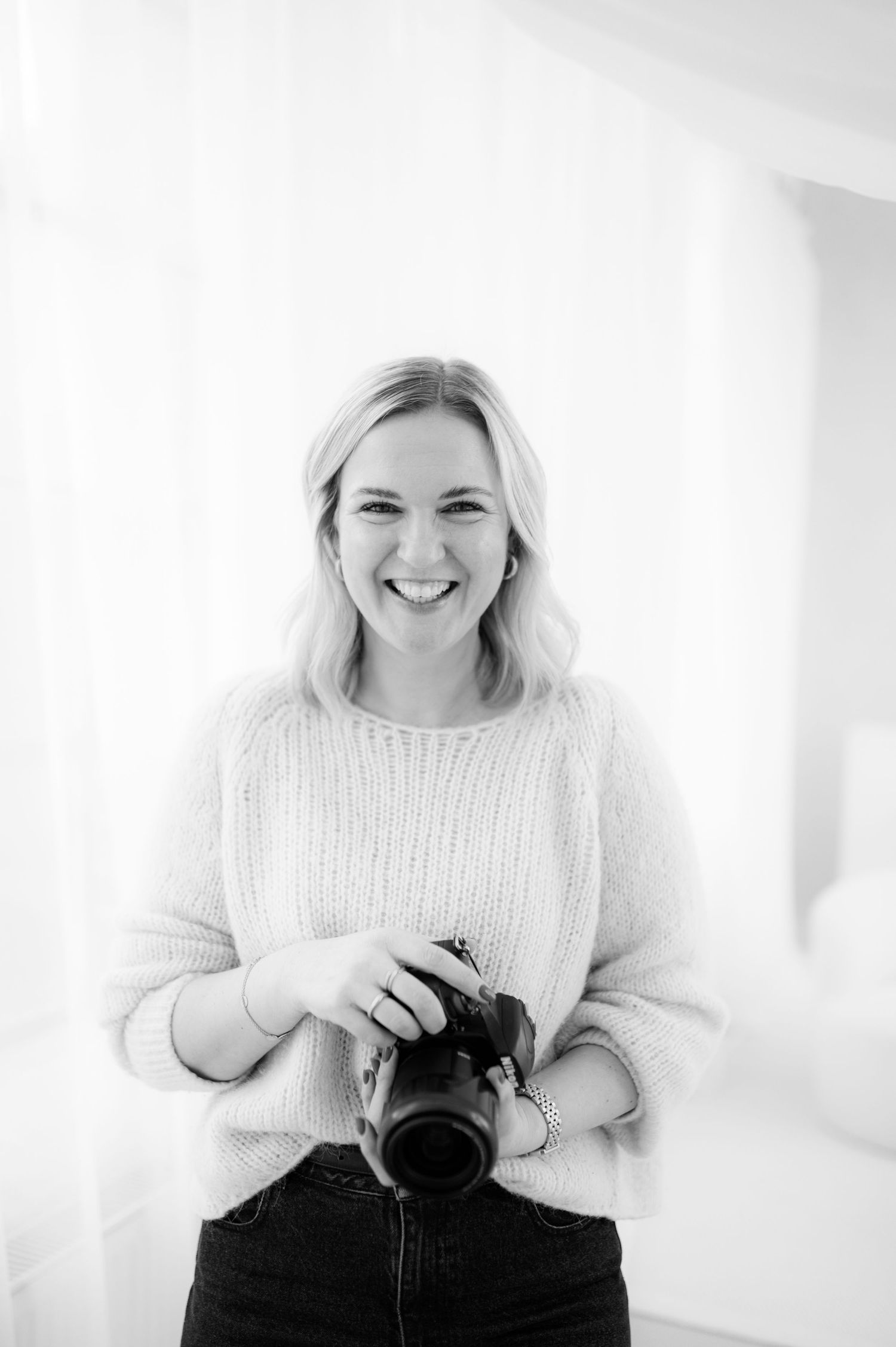 A series of three black and white photos showing someone smiling and holding a camera in a bright studio space.