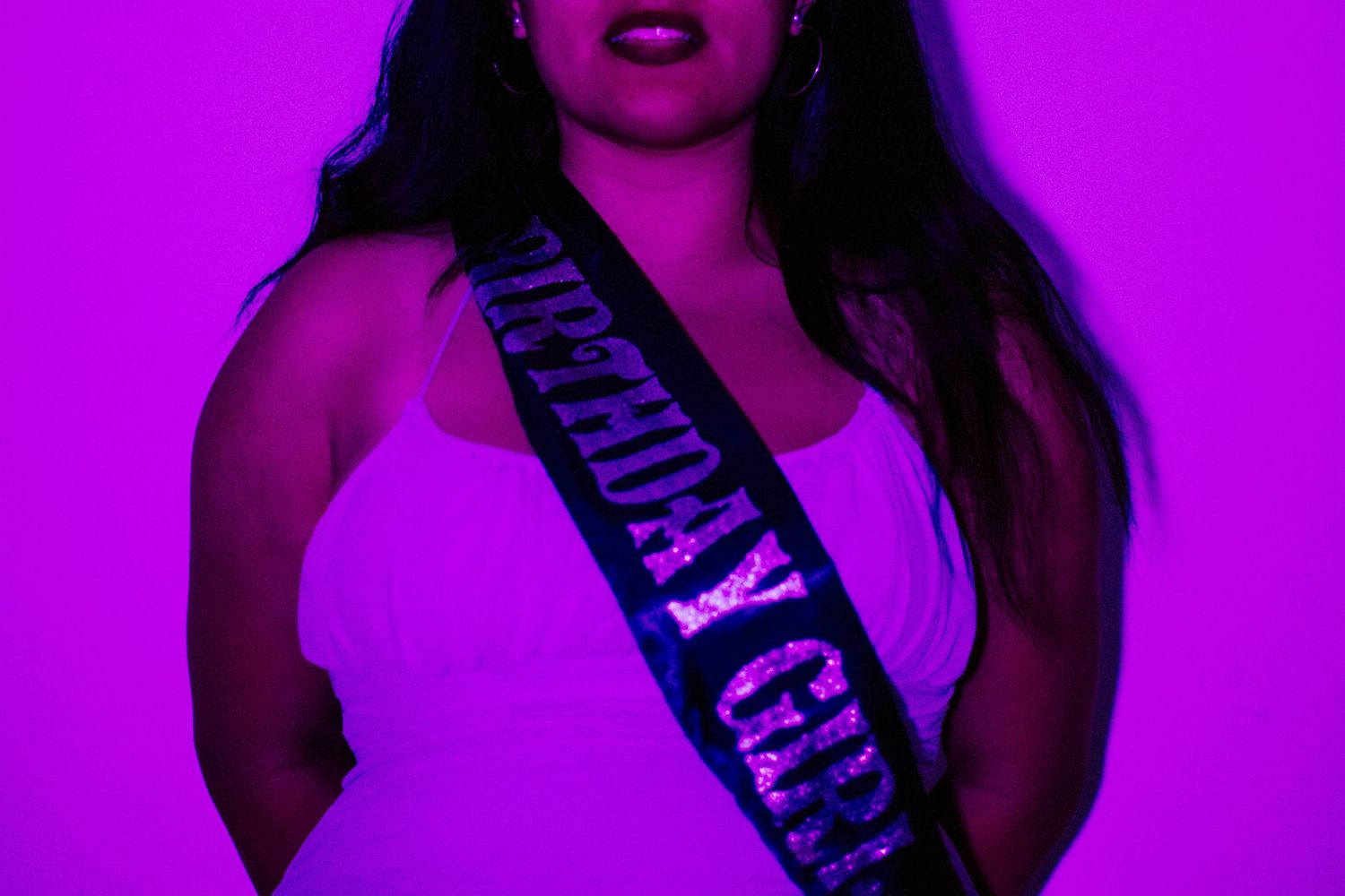 Figure in purple lighting wearing a dark sash with glowing text against neon background.