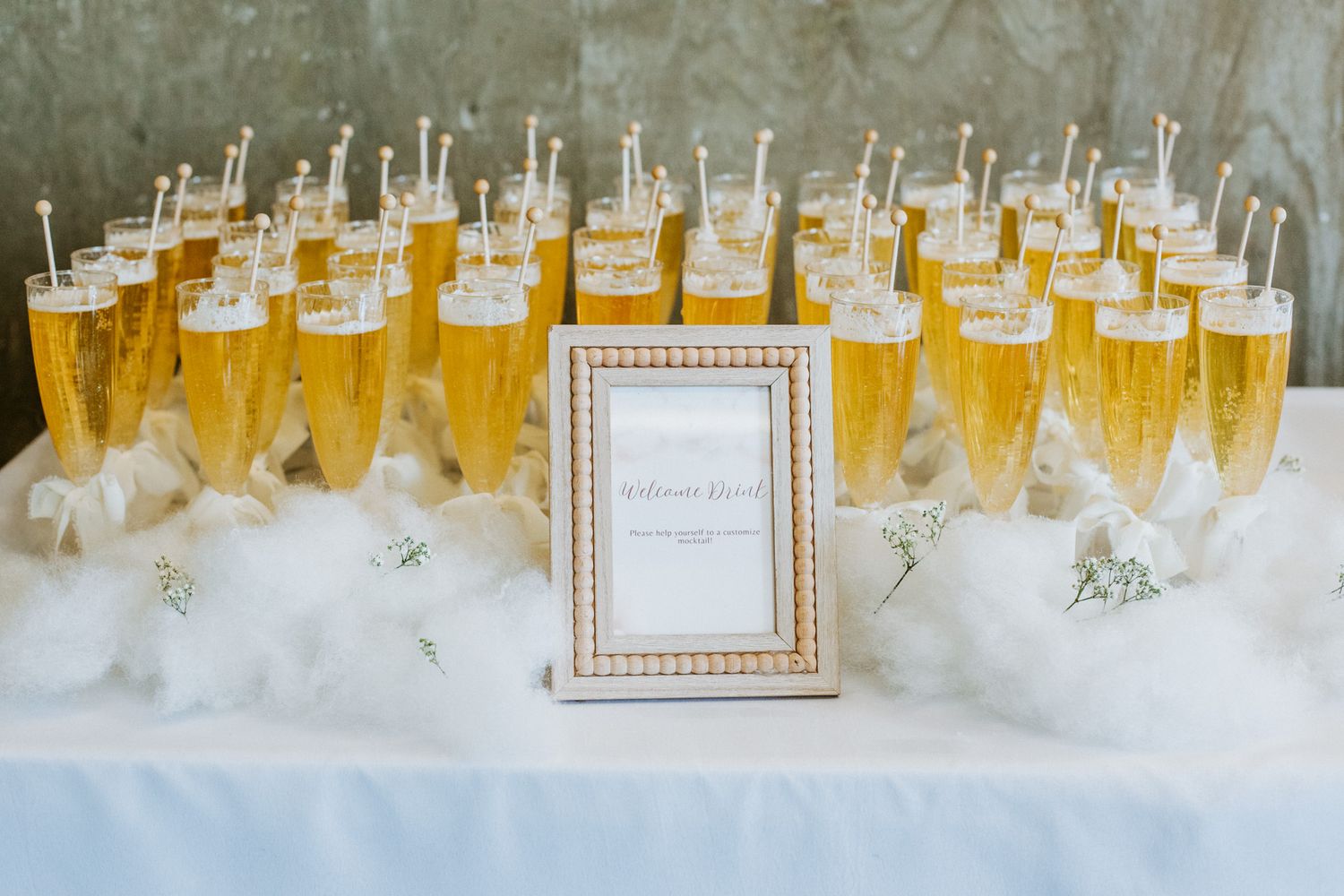 Champagne flutes filled with golden bubbly drinks arranged on white linens with an elegant framed sign display.
