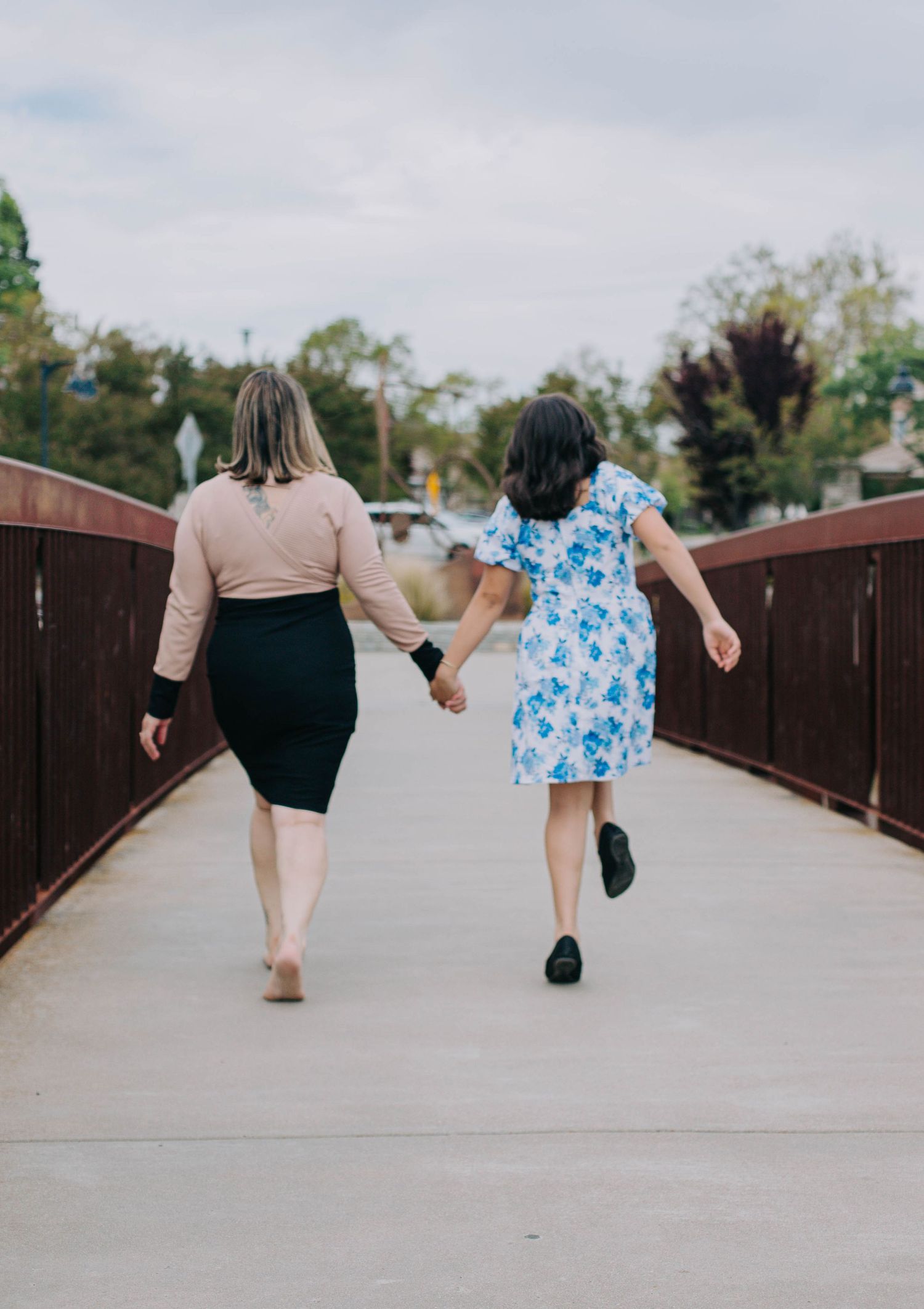 Two people holding hands while walking on a wooden bridge pathway on a cloudy day.