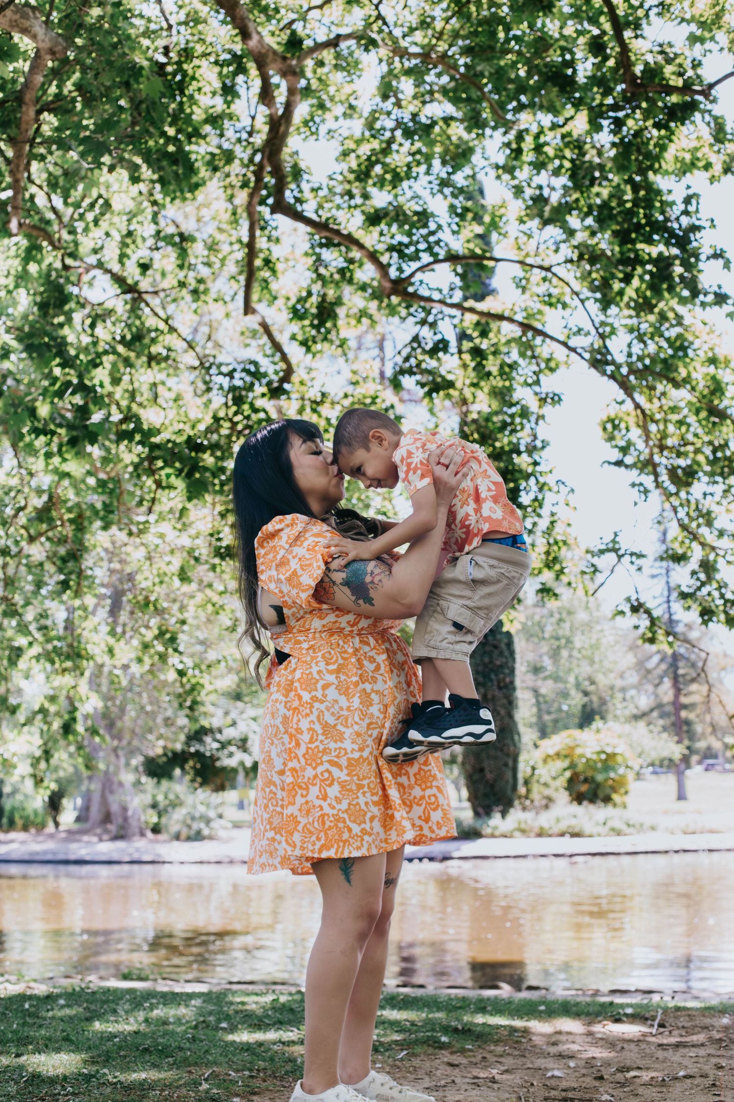 An orange floral dress complements the summer scenery by a lake with overhanging trees providing natural shade.