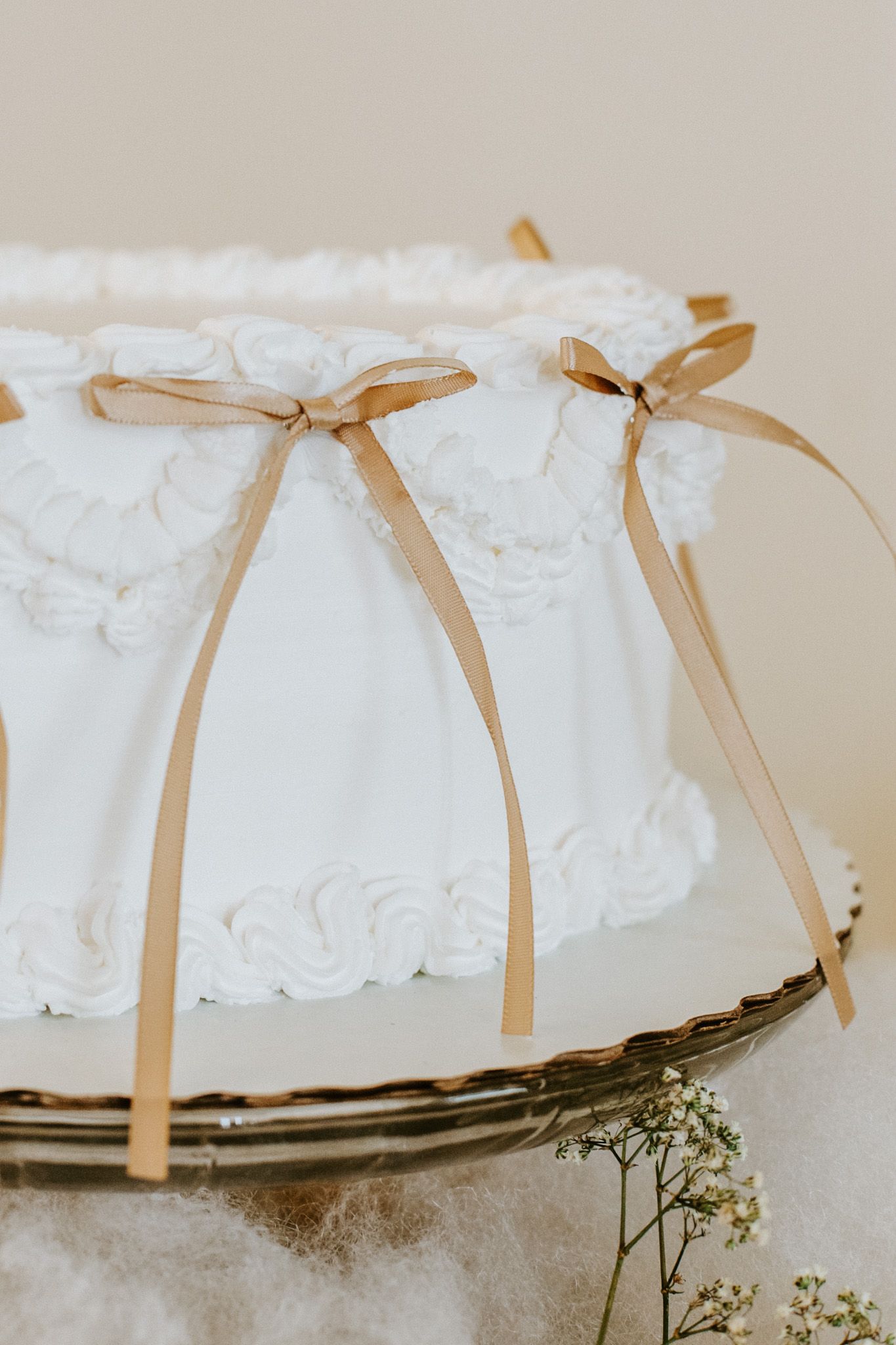 White wedding cake with delicate gold ribbons and bows decorated in vintage style on an antique cake stand.