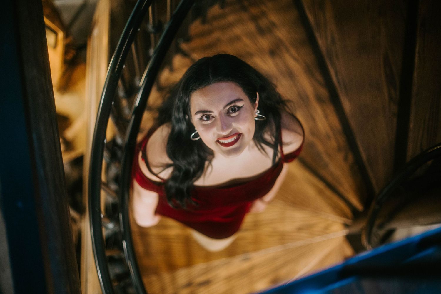 Looking up through a spiral staircase at someone wearing red against a warm golden background.