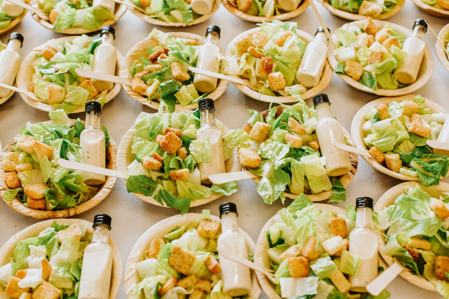 Multiple individual appetizer-sized taco boats with shredded lettuce, cheese, and toppings arranged in neat rows for catering.