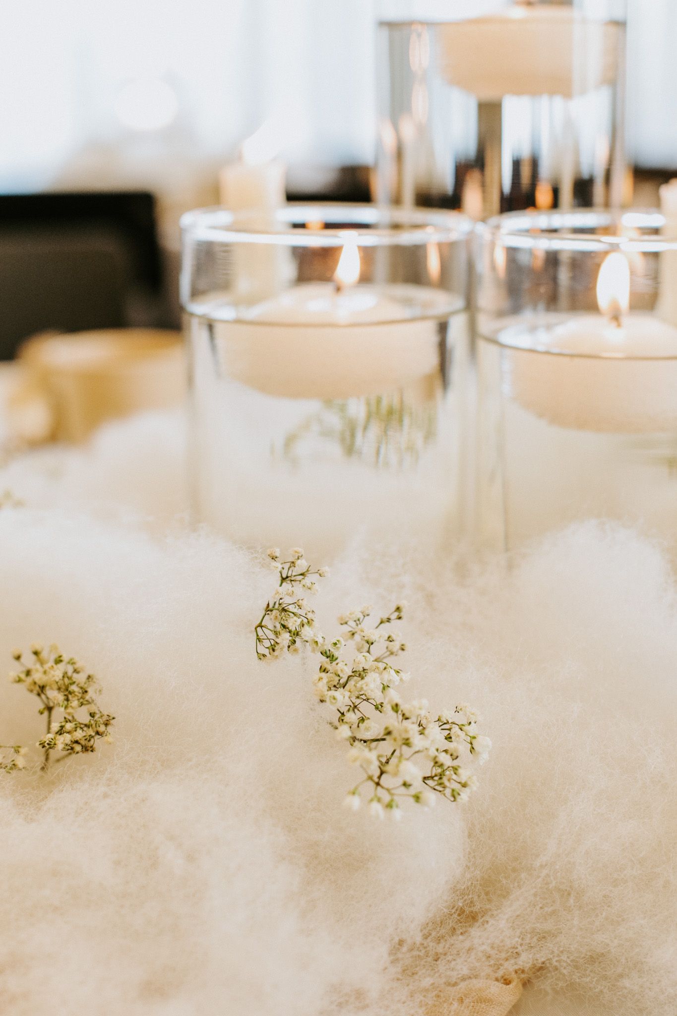 Soft white candles in glass holders set among delicate baby's breath and ethereal cotton-like decorative elements.