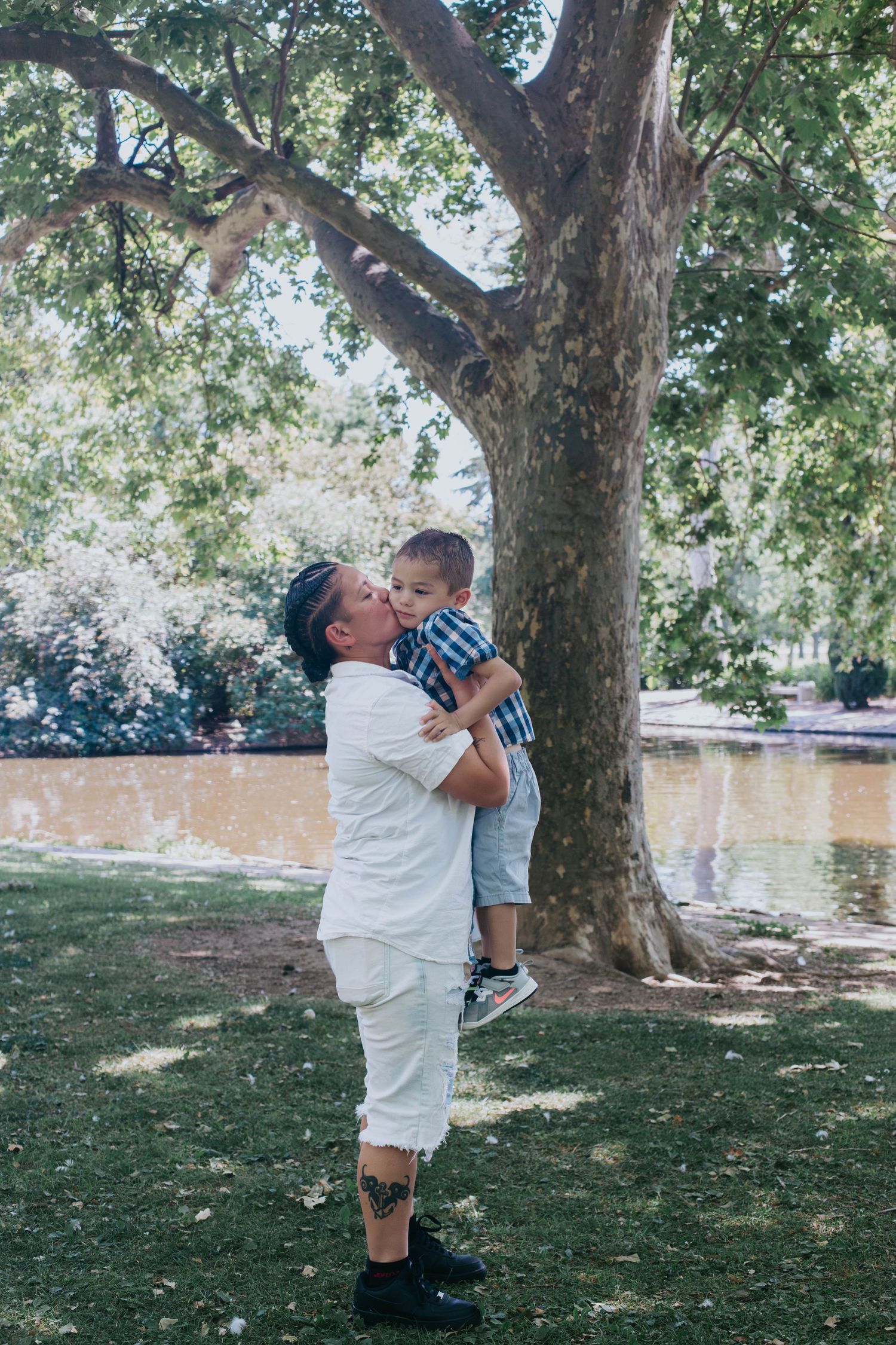 A tender moment shared between two people under a large tree in a peaceful park setting on a sunny day.