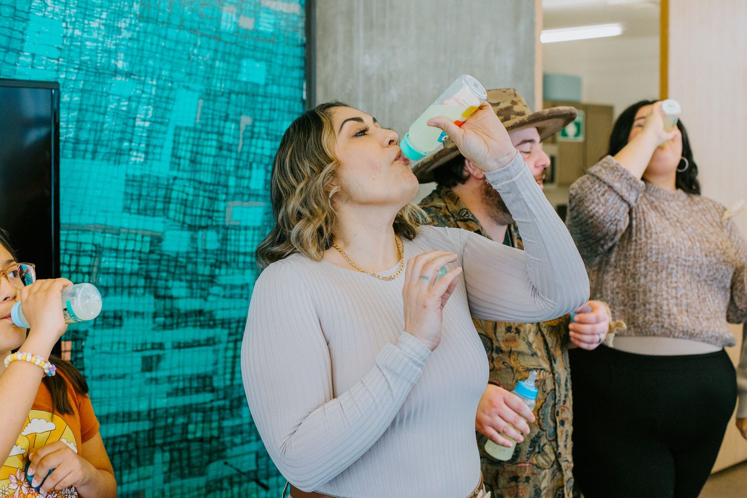 People enjoying beverages at a party with a light blue wall backdrop and casual gathering atmosphere.