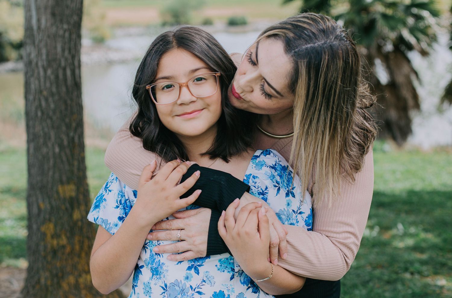Two people embrace outdoors in a loving moment wearing blue floral and pink outfits against a natural background.