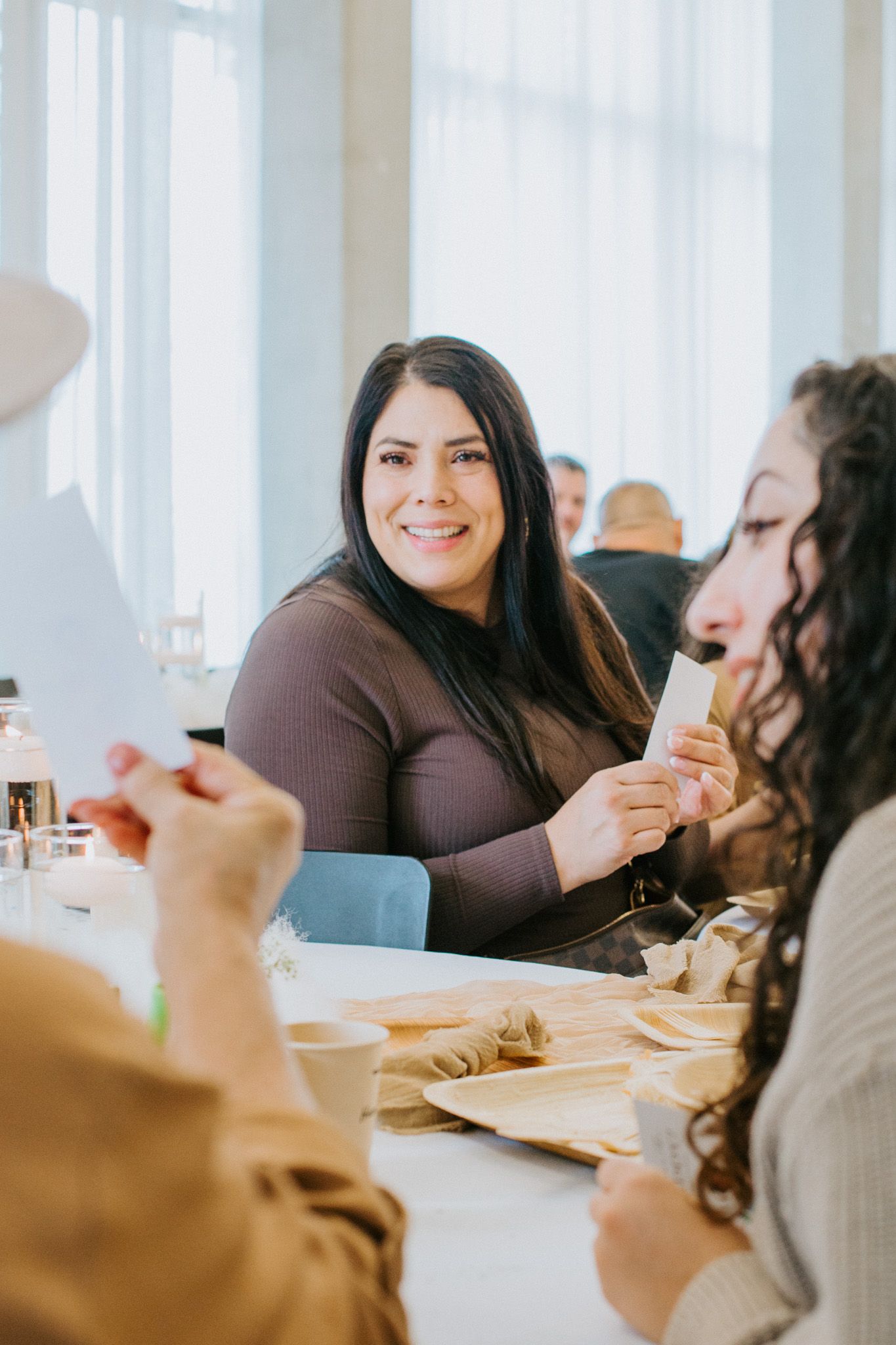 Friends gather around a bright dining table enjoying drinks and conversation during a casual meal together.