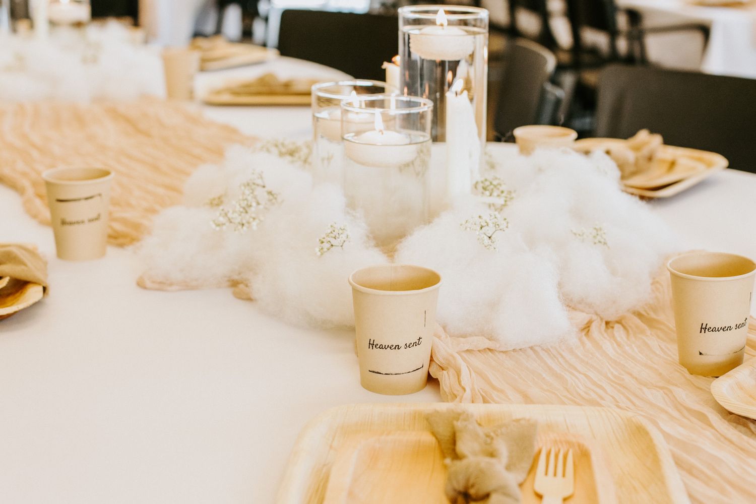 An elegant wedding reception table setting with white tulle decor, glassware and disposable coffee cups on a tablecloth.