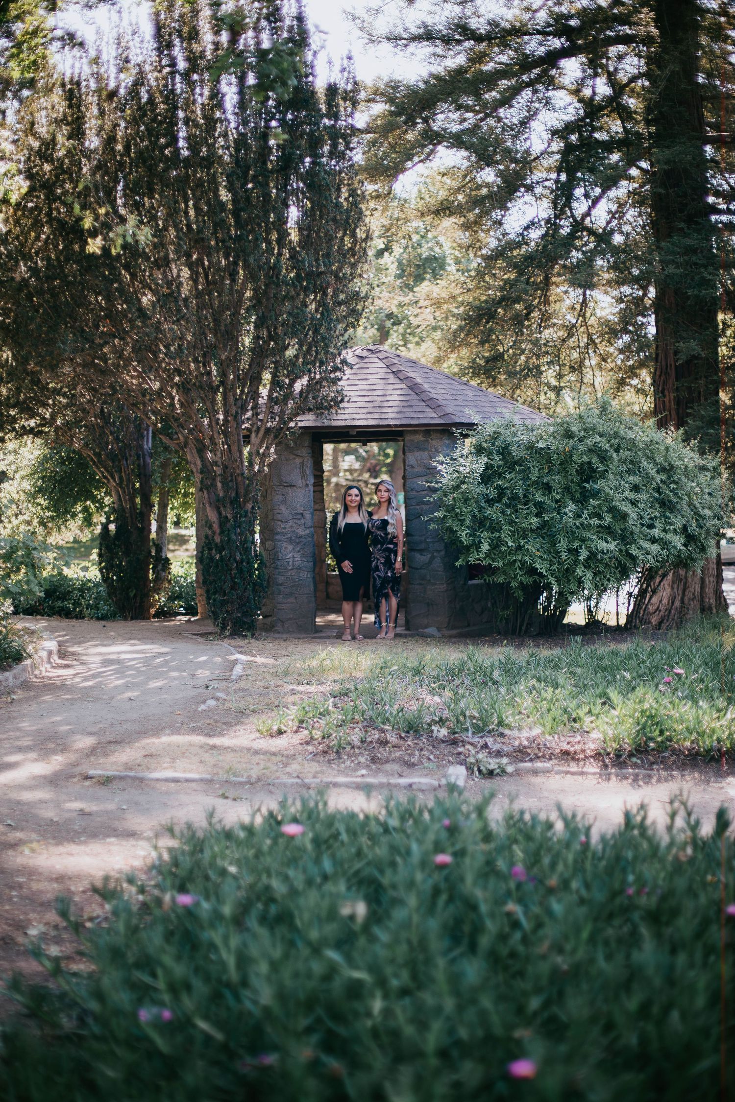 Small rustic wooden shelter nestled among trees and greenery in a peaceful garden setting.