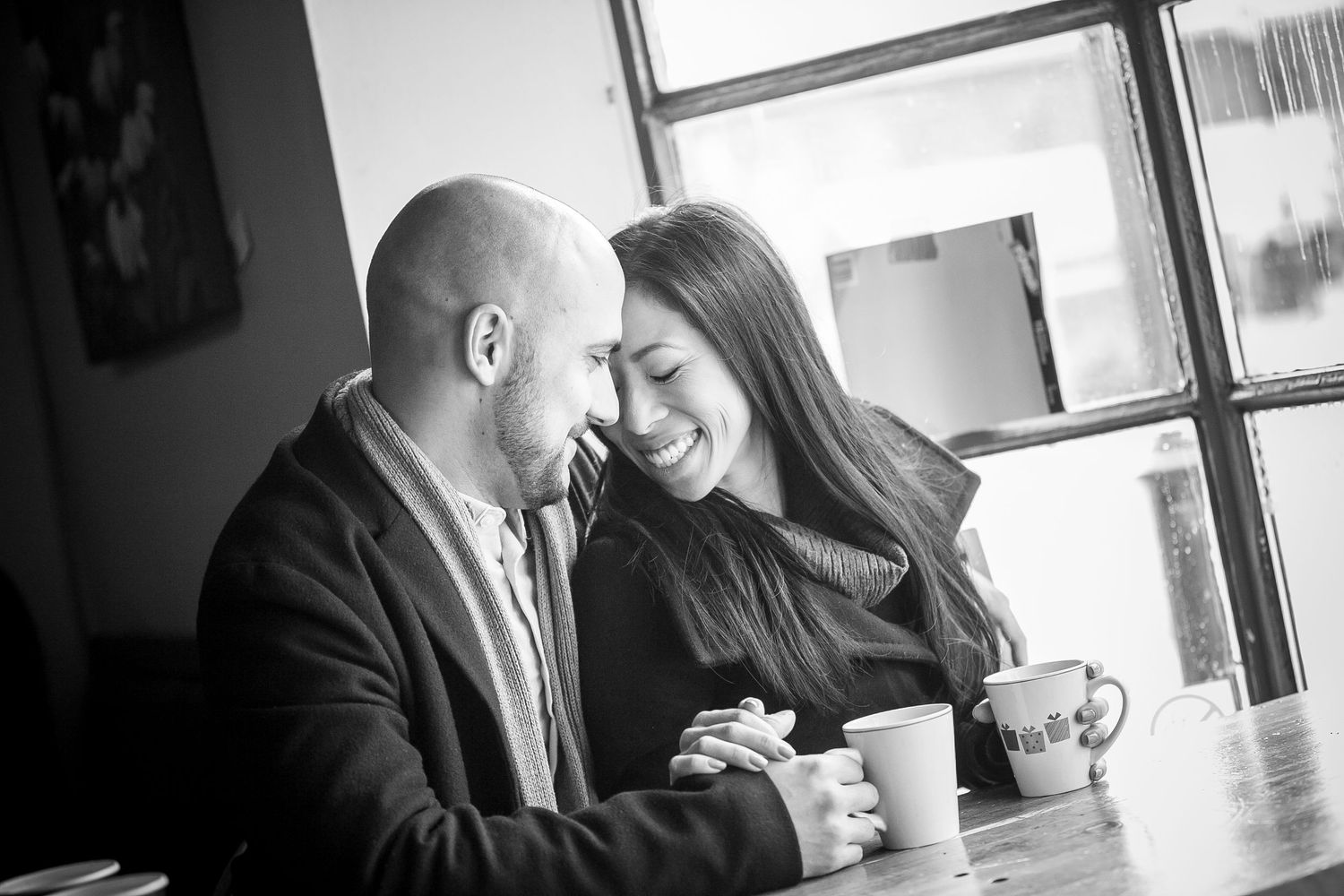 Black and white photo of a smiling couple sharing an intimate moment over coffee at a cafe table.