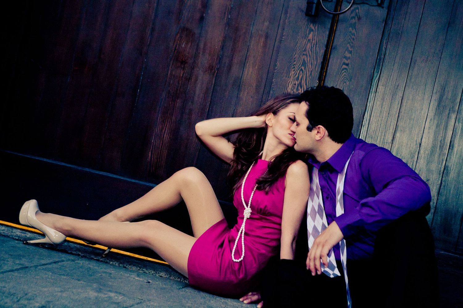 Couple in purple outfits sharing a romantic moment while sitting on the ground against a wooden door.