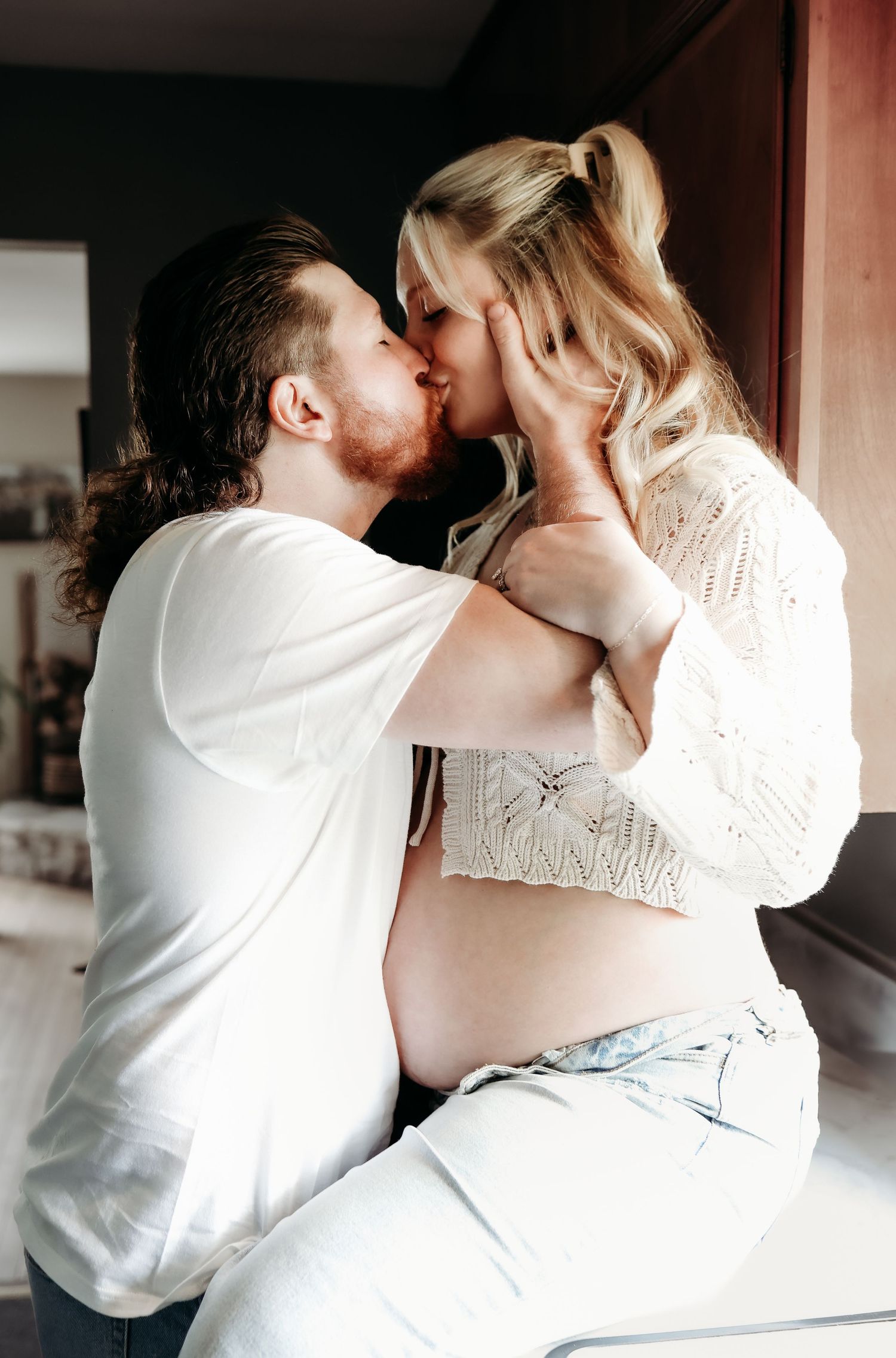 Expecting couple sharing a romantic kiss during an indoor maternity photo session.
