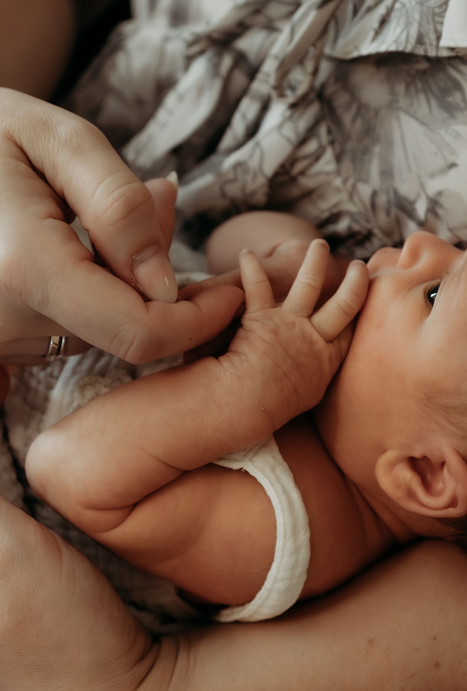 Close-up of adult hands gently holding newborn baby's tiny fingers on soft blanket.