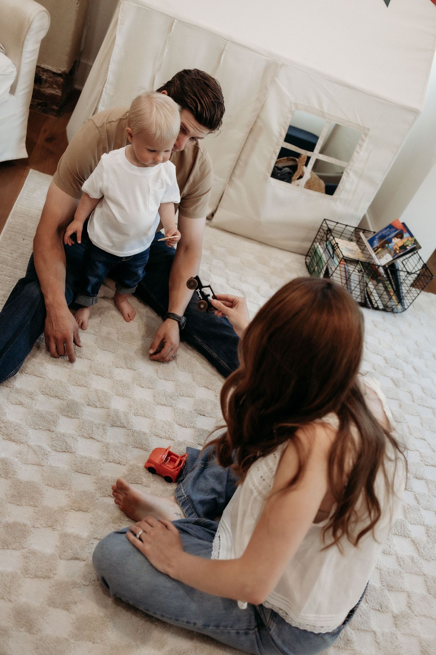 Young parents playing with their baby on a white carpet in a cozy nursery room.