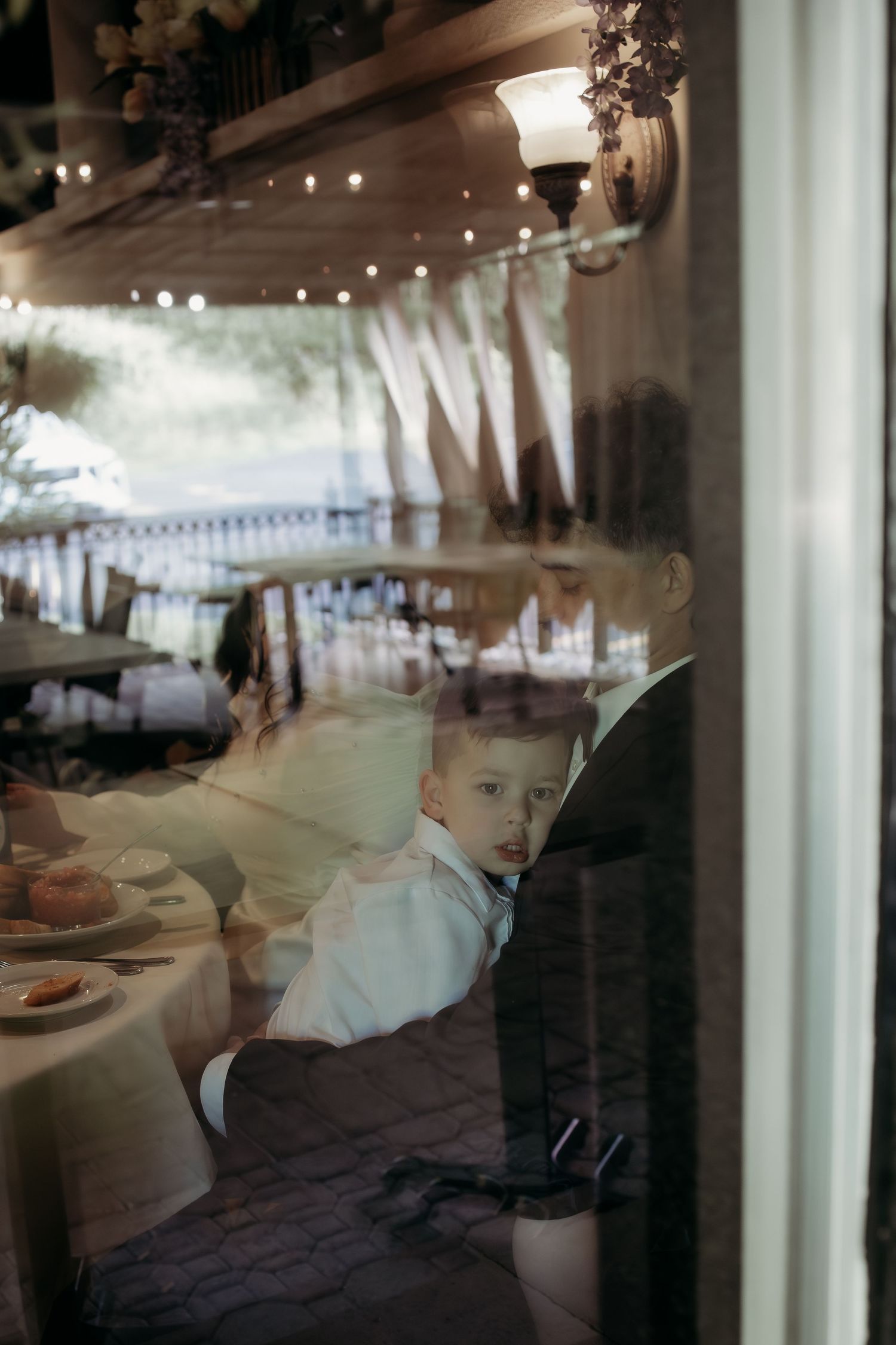 Young child in white shirt seen through a window at an elegant wedding reception venue.