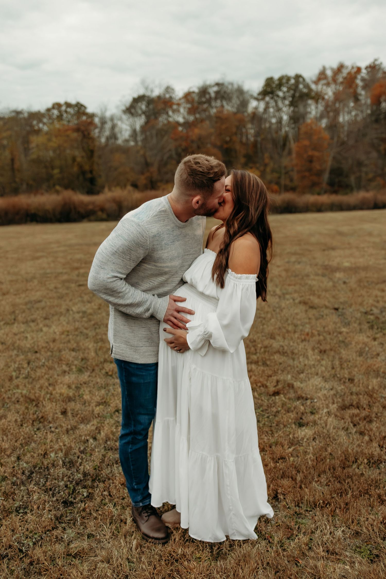 Couple kissing in autumn field, man holding pregnant woman's belly.