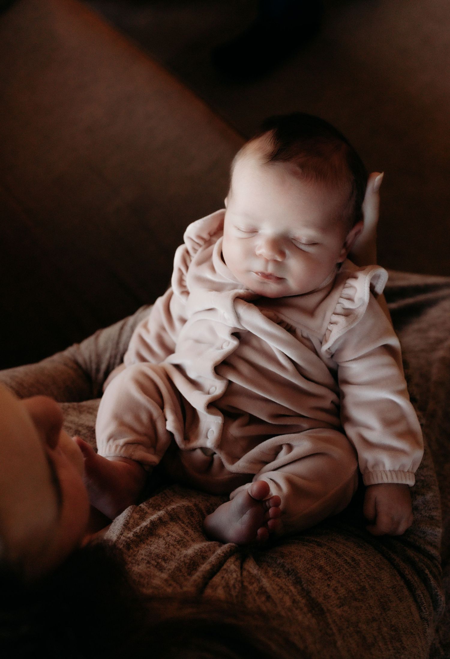 Peaceful newborn baby sleeping in pink ruffle romper cradled in loving arms.