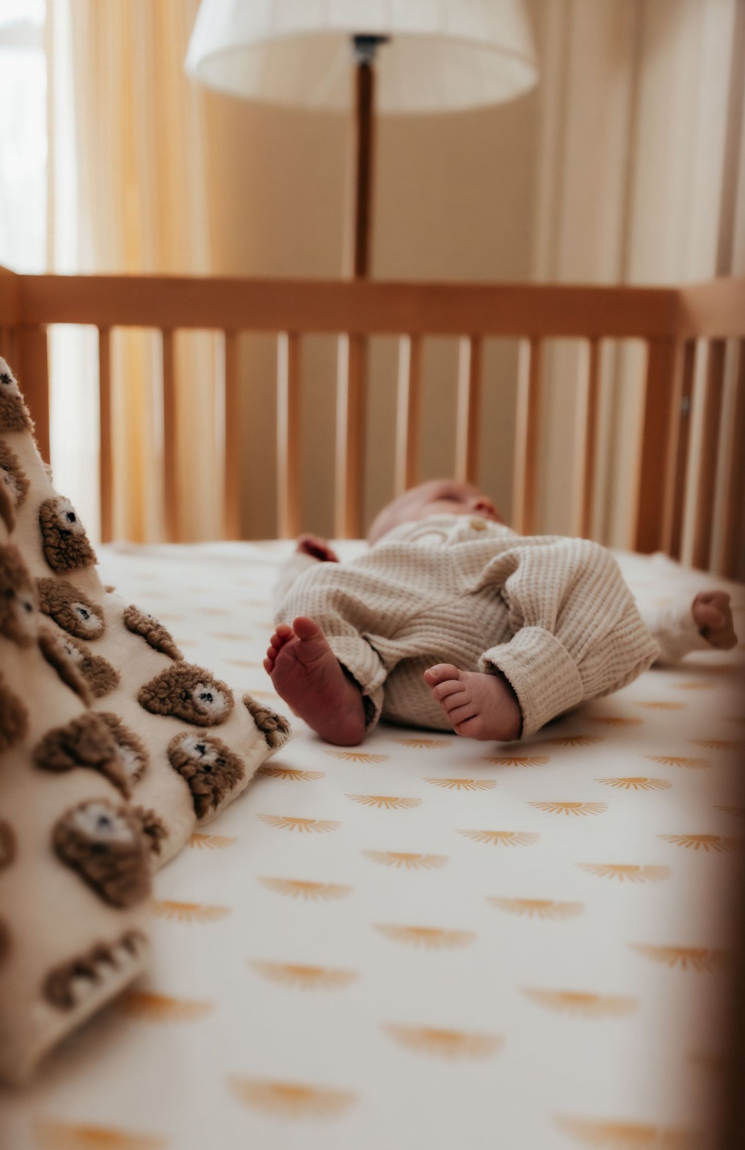 Newborn baby in striped outfit lying in wooden crib with bear-themed bedding.