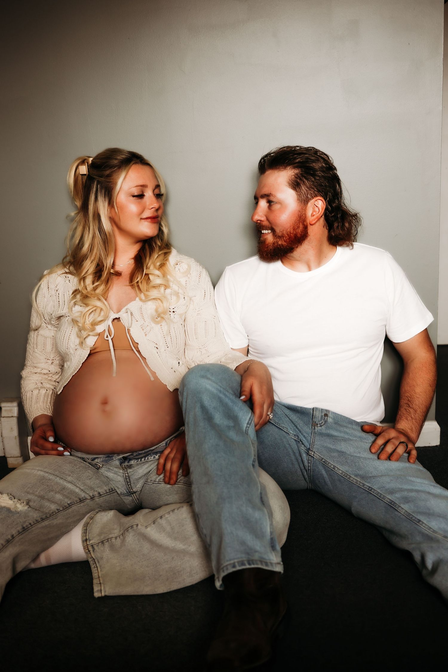 Couple lounging together on dark surface in casual white and denim outfits.