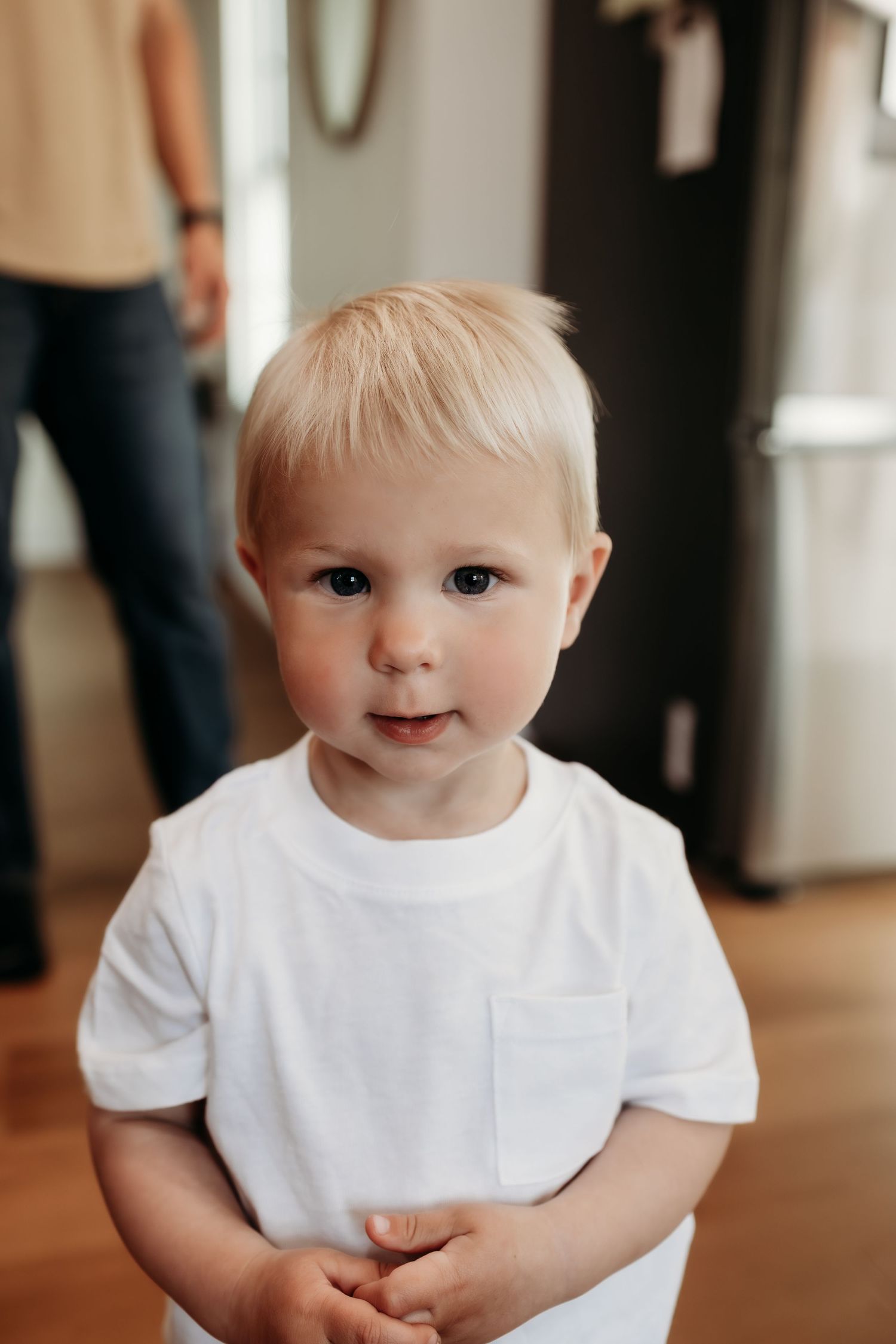 Cute blonde toddler boy in white t-shirt looking at camera indoors.