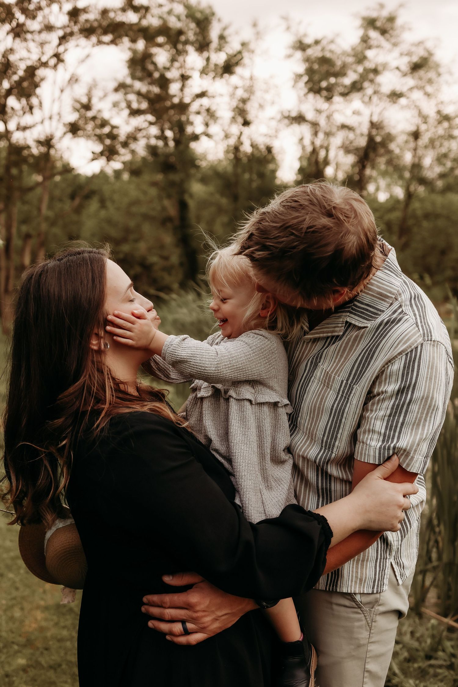 A happy family with a toddler shares a warm embrace in a lush green park.