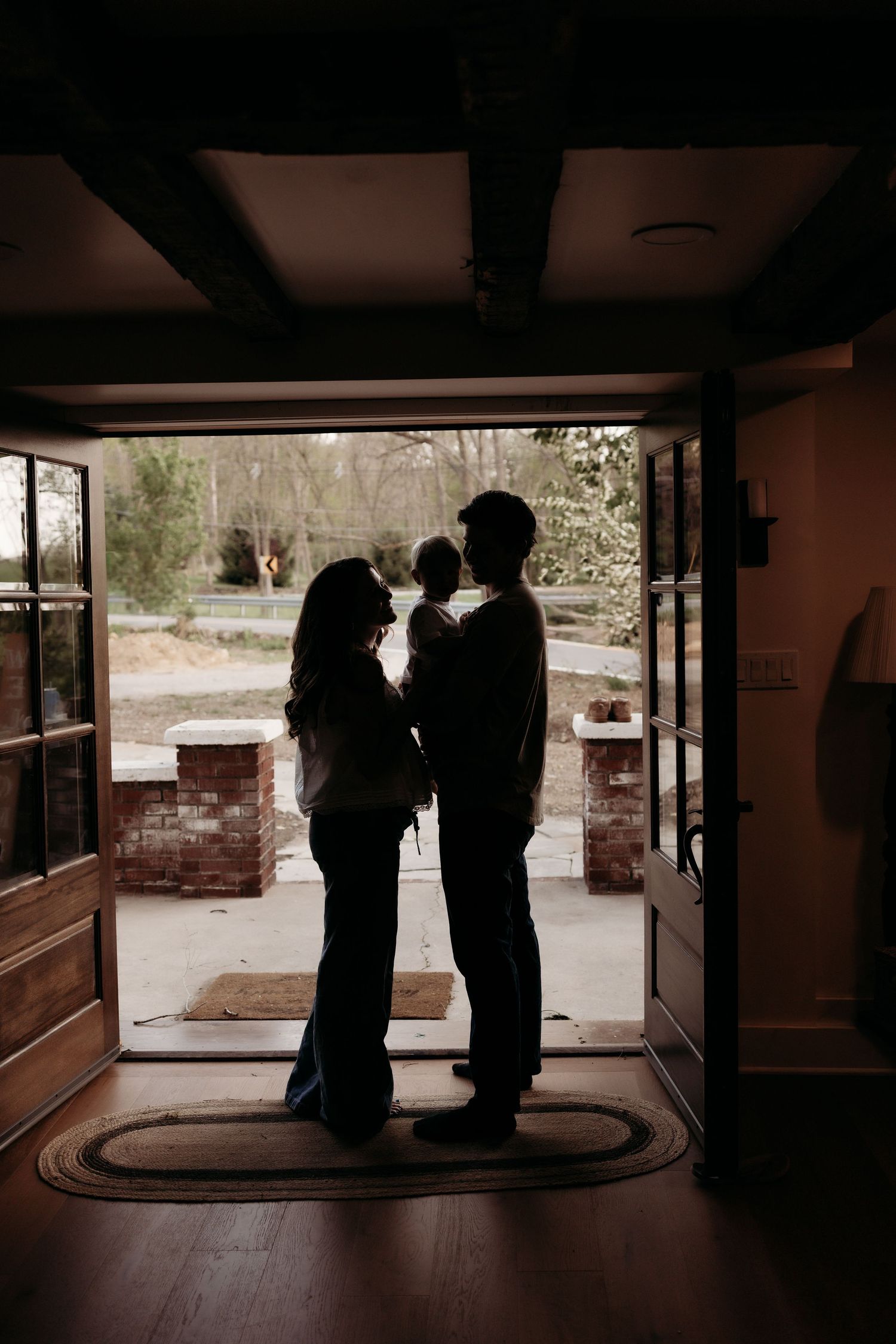 Silhouette of a couple holding a baby standing in an open doorway with trees visible outside.