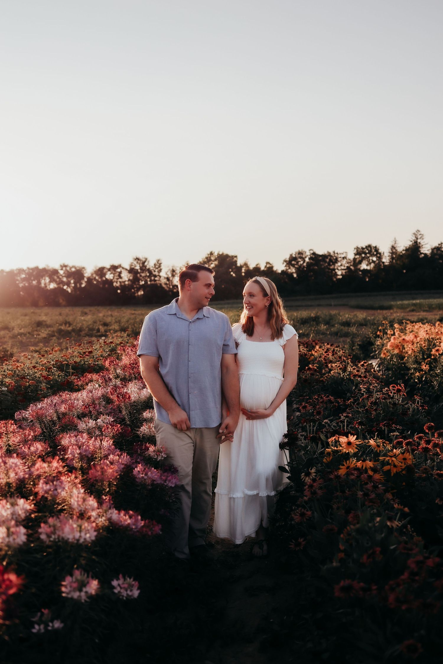 Expecting couple standing together in a colorful flower field during a warm sunset maternity photo session.