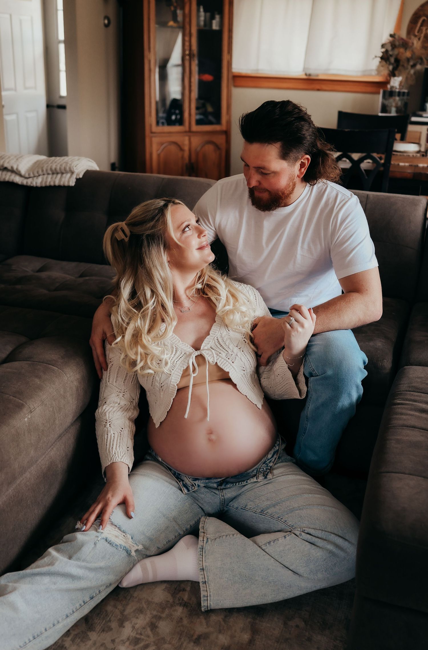 Pregnant woman and partner sharing a joyful moment sitting together on a couch.