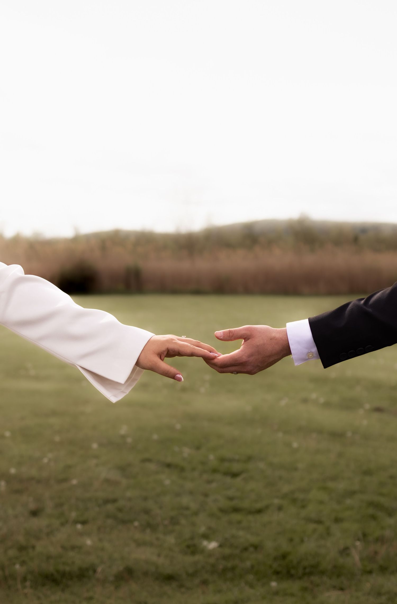 Close-up of bride and groom reaching for each other's hands in a romantic outdoor wedding moment.