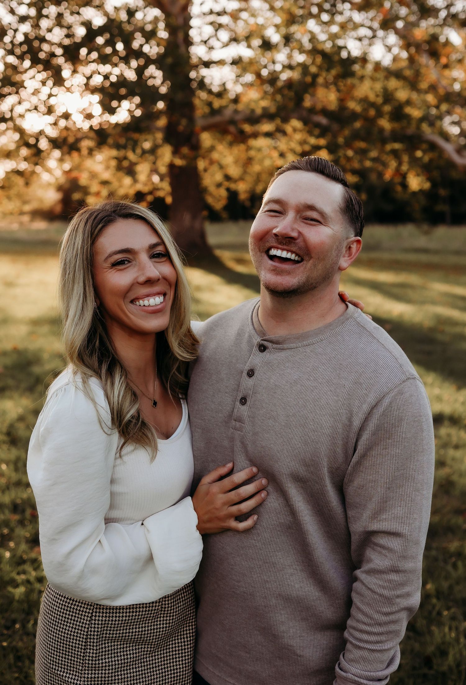 Happy couple laughing together outdoors during golden hour in a lush green park.