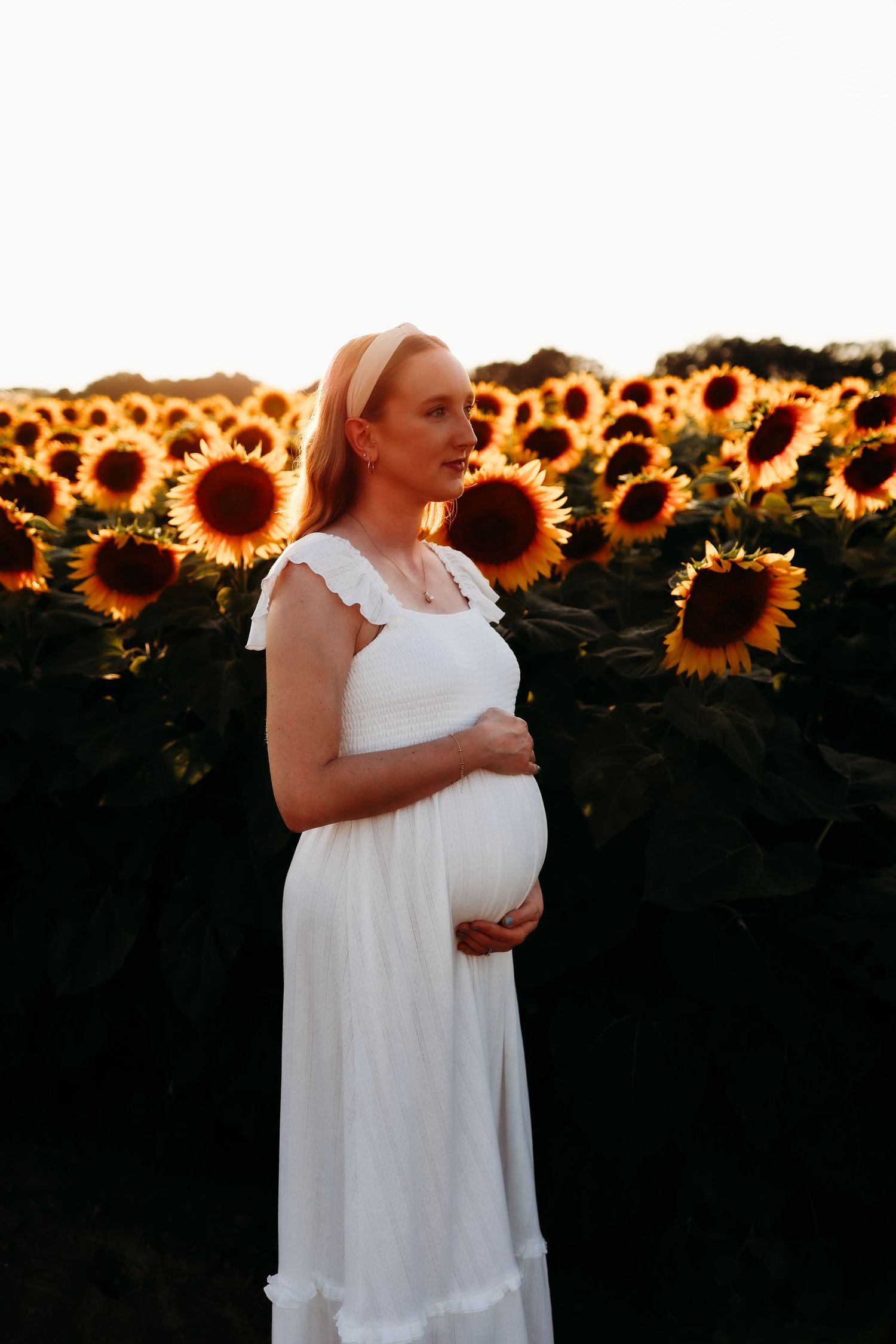 Woman having a tender moment at sunset in a blooming sunflower field at Tranquility farms in Andover, New Jersey maternity shoot