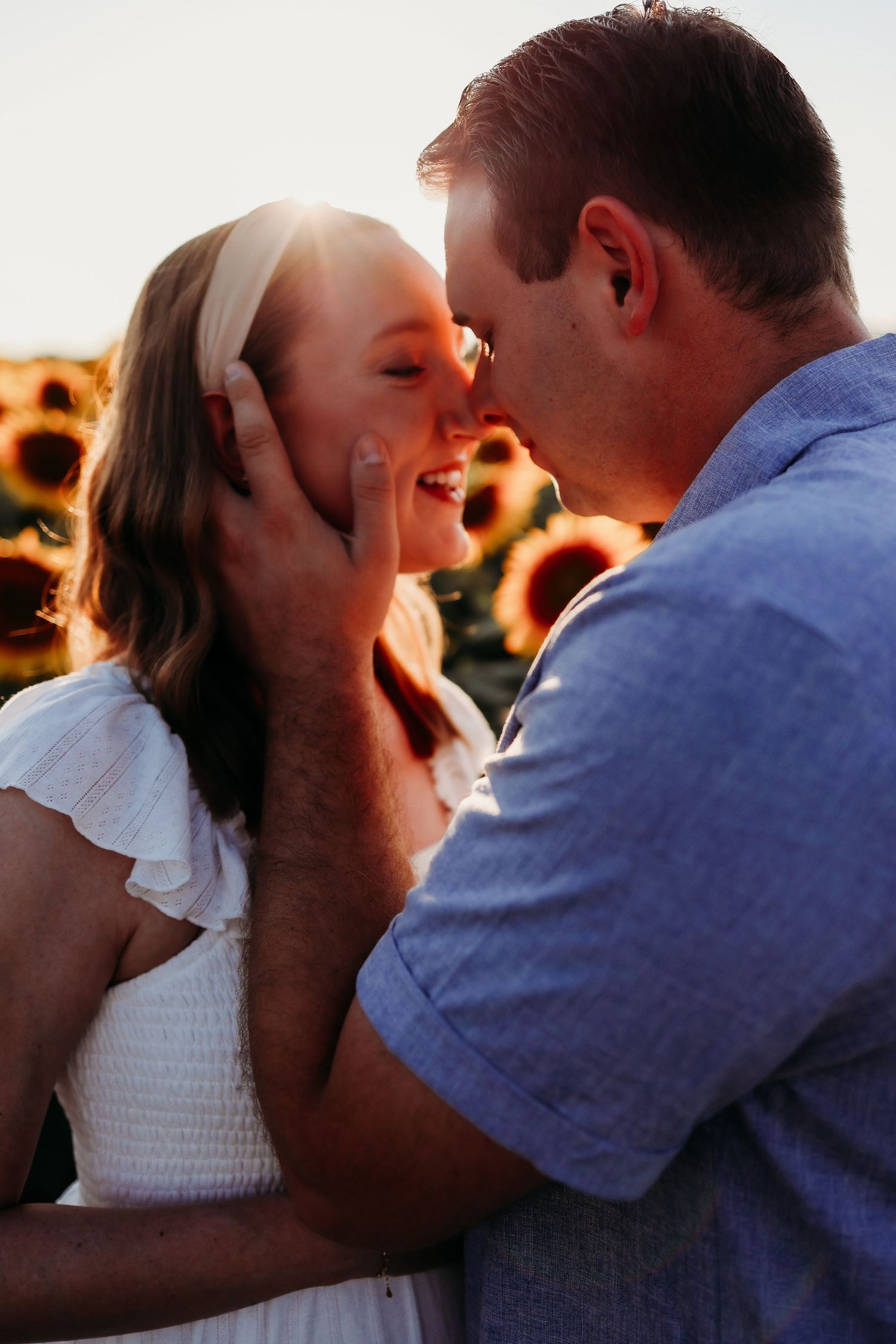 Romantic couple kissing in a sunflower field during a maternity session in Newton, New Jersey at sunset with warm golden lighting.