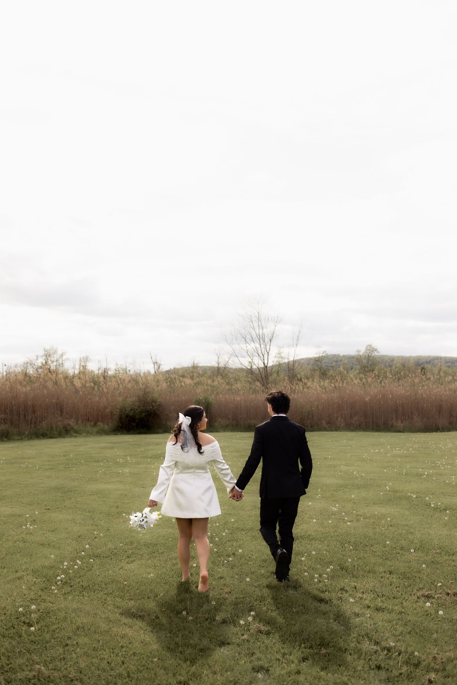 Bride and groom holding hands walking across a green field on their wedding day.