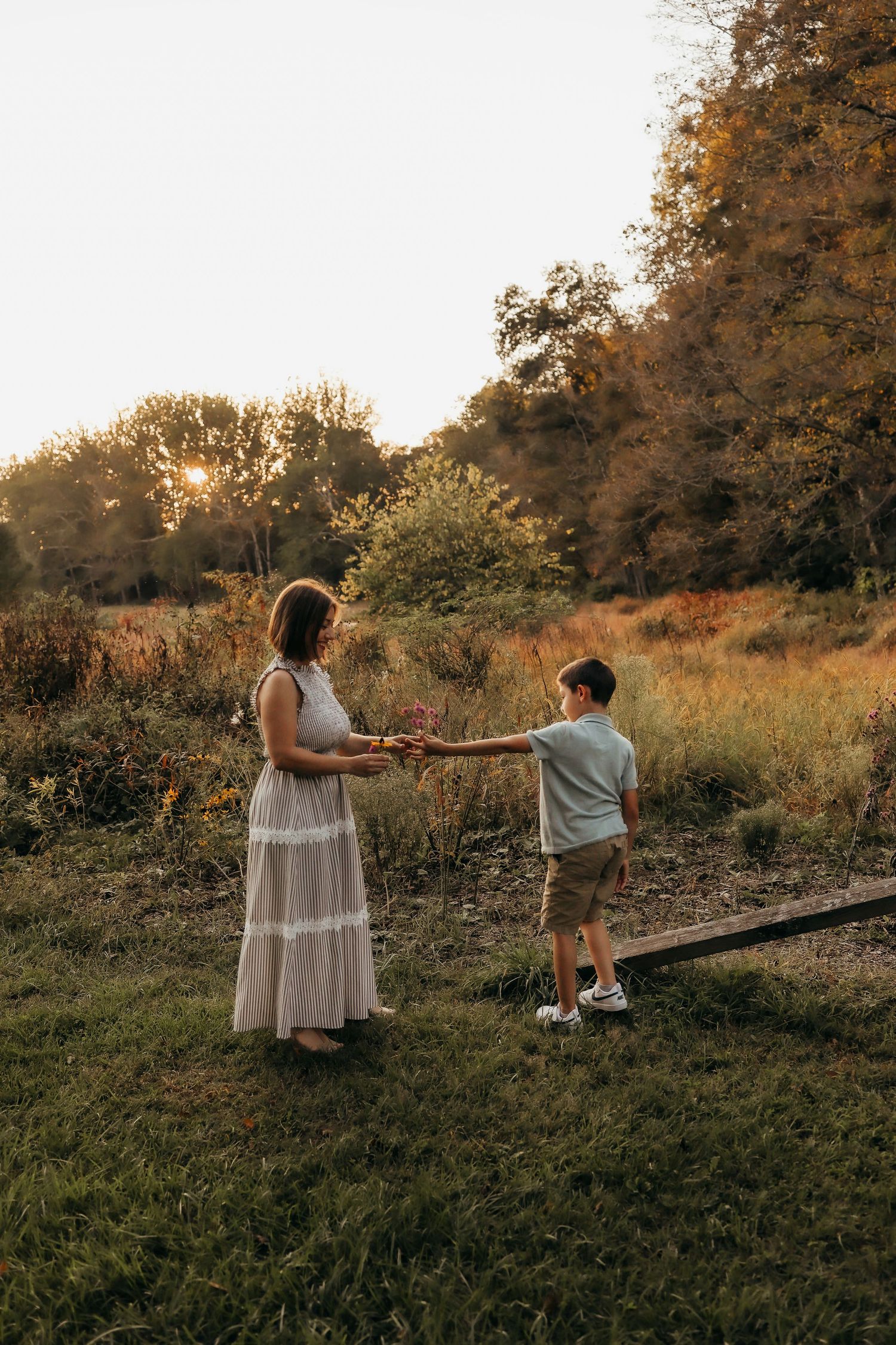 Mother and son share flowers together in a golden sunset meadow during an outdoor family session.