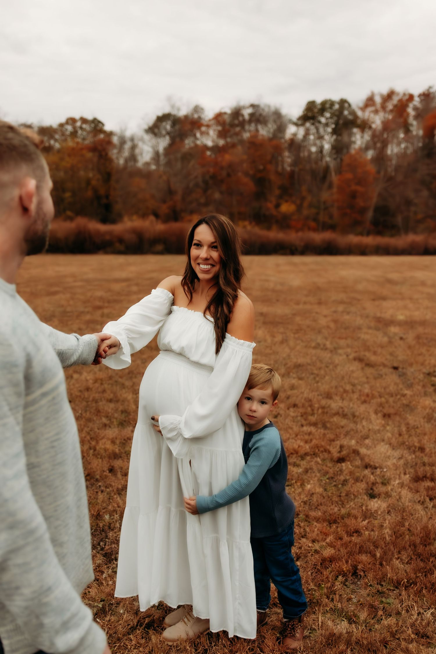 A sweet autumn family moment captured in a field with warm fall colors and trees in the background.