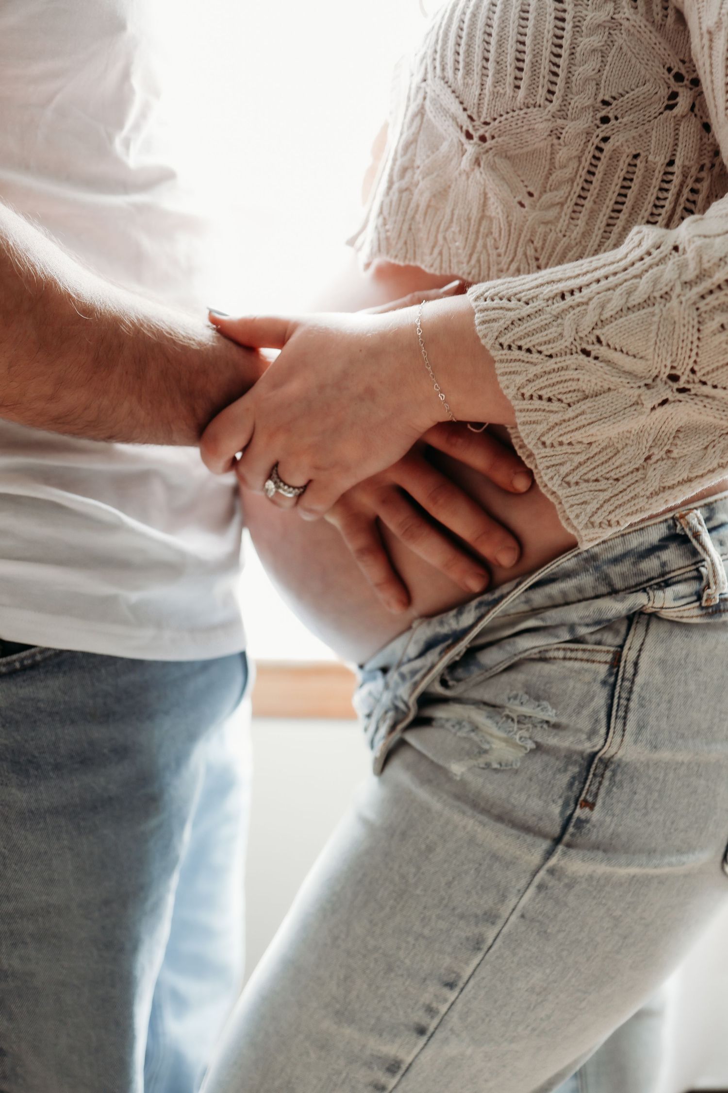 Close-up of couple's hands resting on pregnant woman's baby bump in jeans.