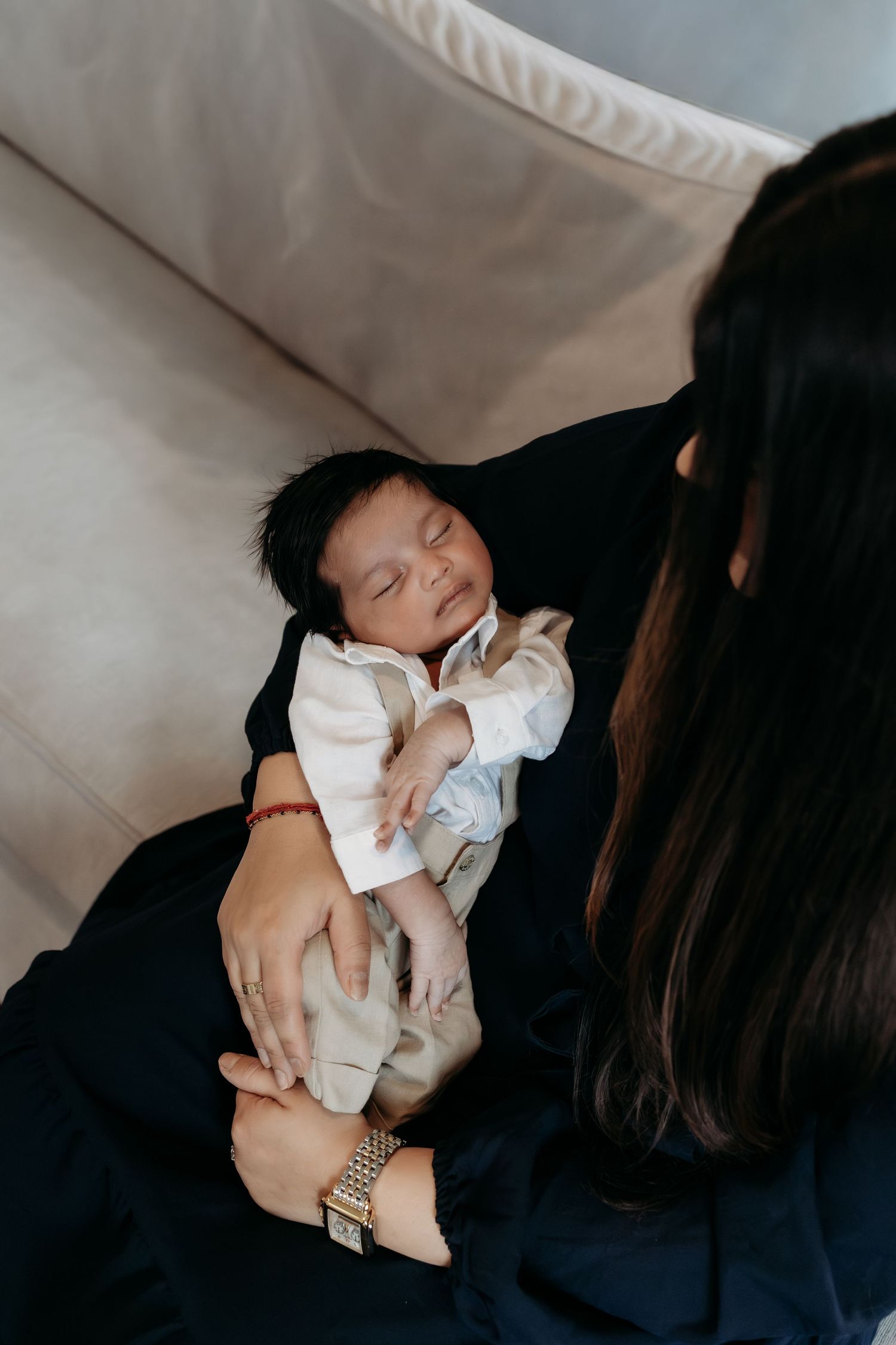A dark-haired newborn baby sleeps in mothers arms while she gazes lovingly from above.