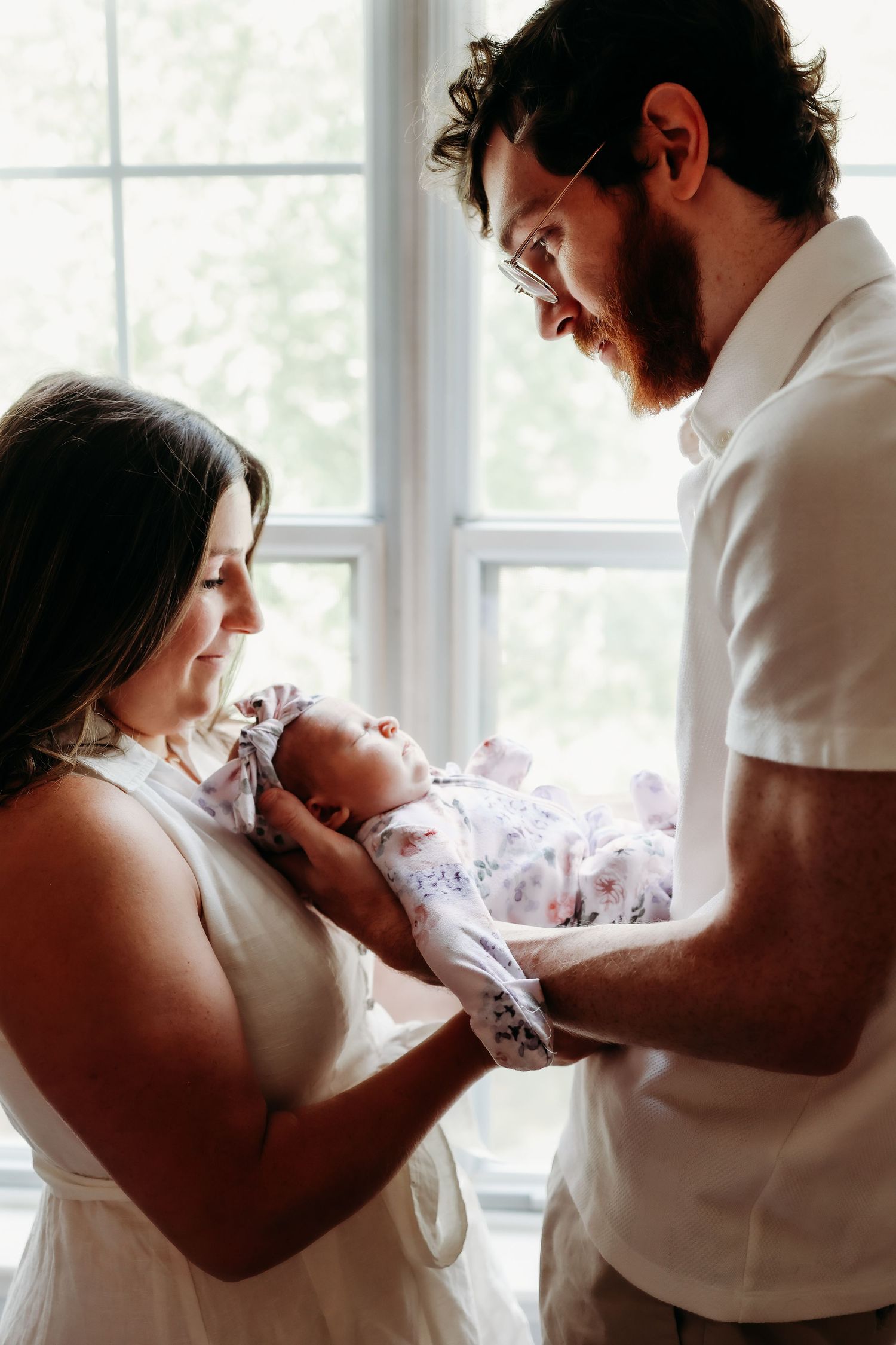 A series of intimate black and white photos showing tender moments between parents and their newborn baby by a window.
