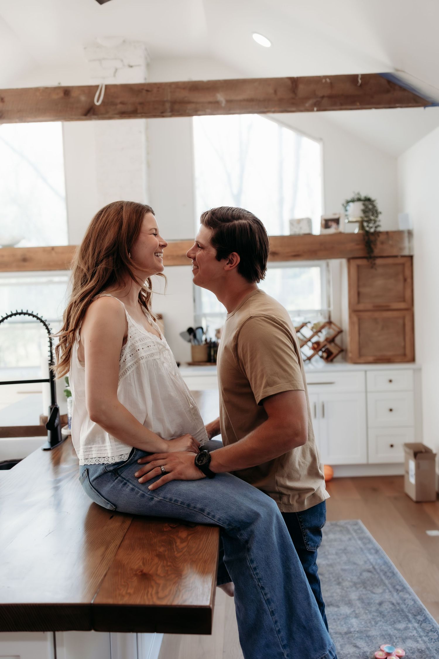A happy couple shares a romantic moment in a modern farmhouse kitchen, woman sitting on wooden counter.