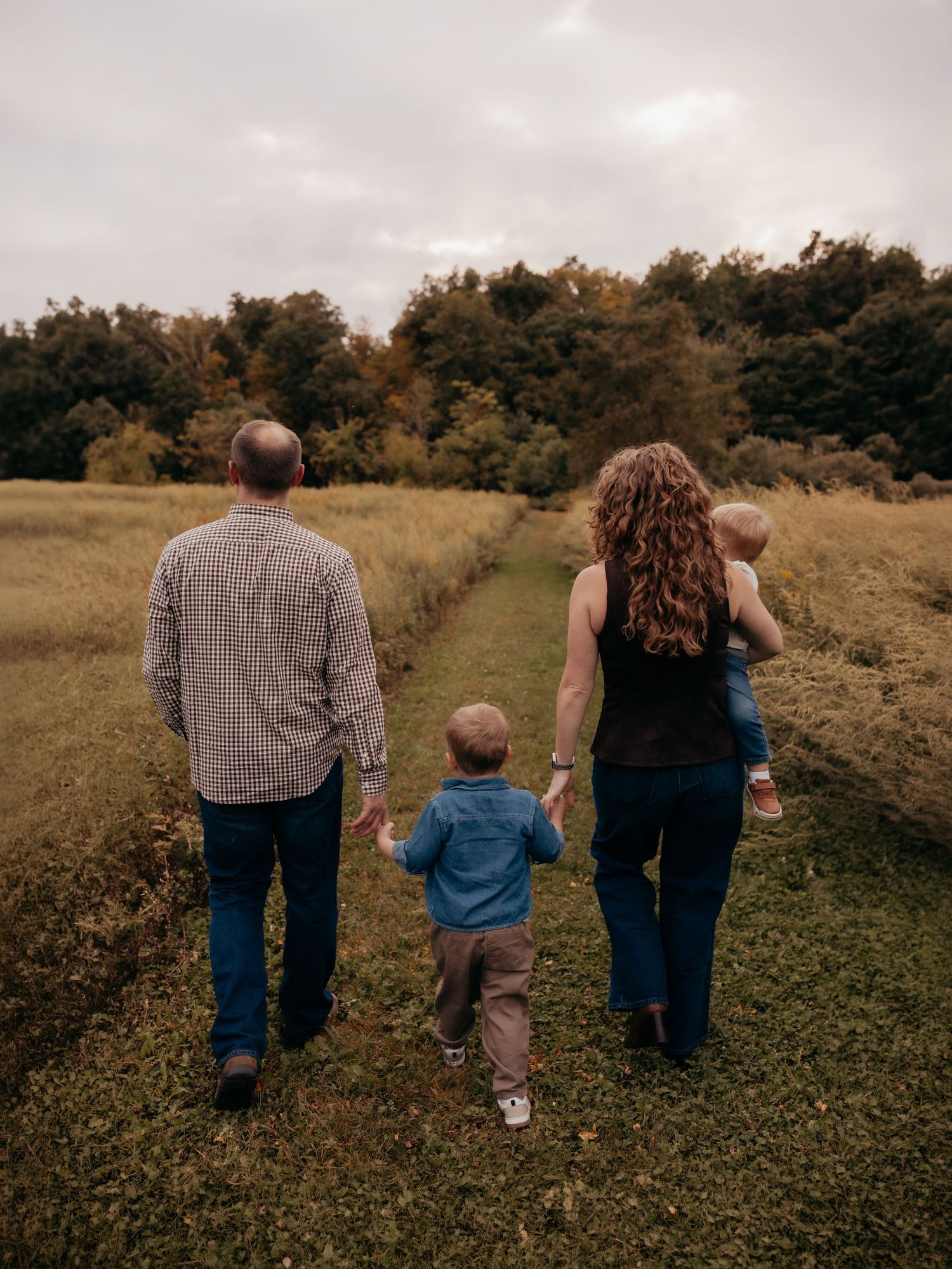 Family of four walking away down a grassy path surrounded by fall foliage on an overcast day.
