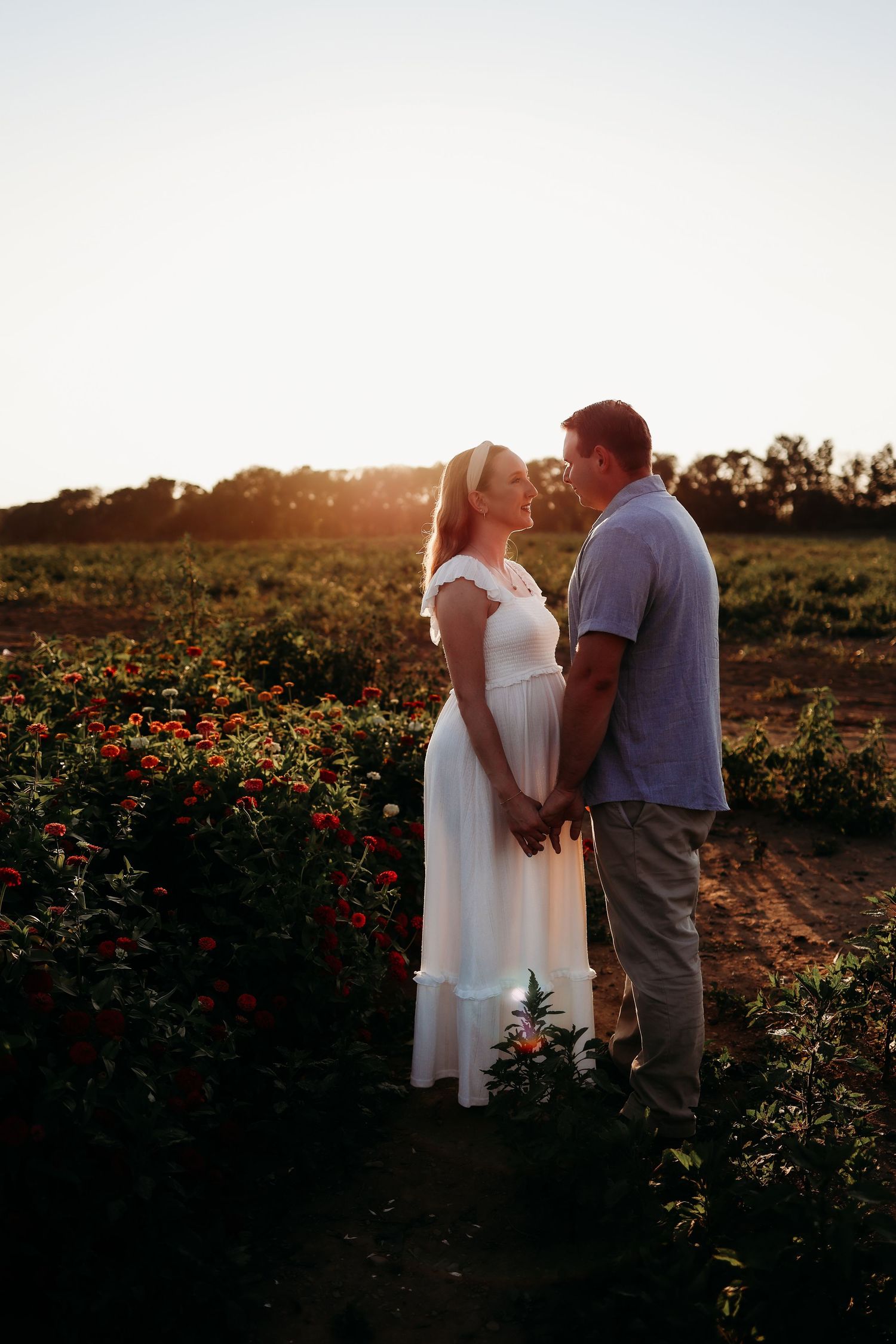 Couple shares tender moment in beautiful flower garden during warm sunset glow in Sussex County, NJ maternity session