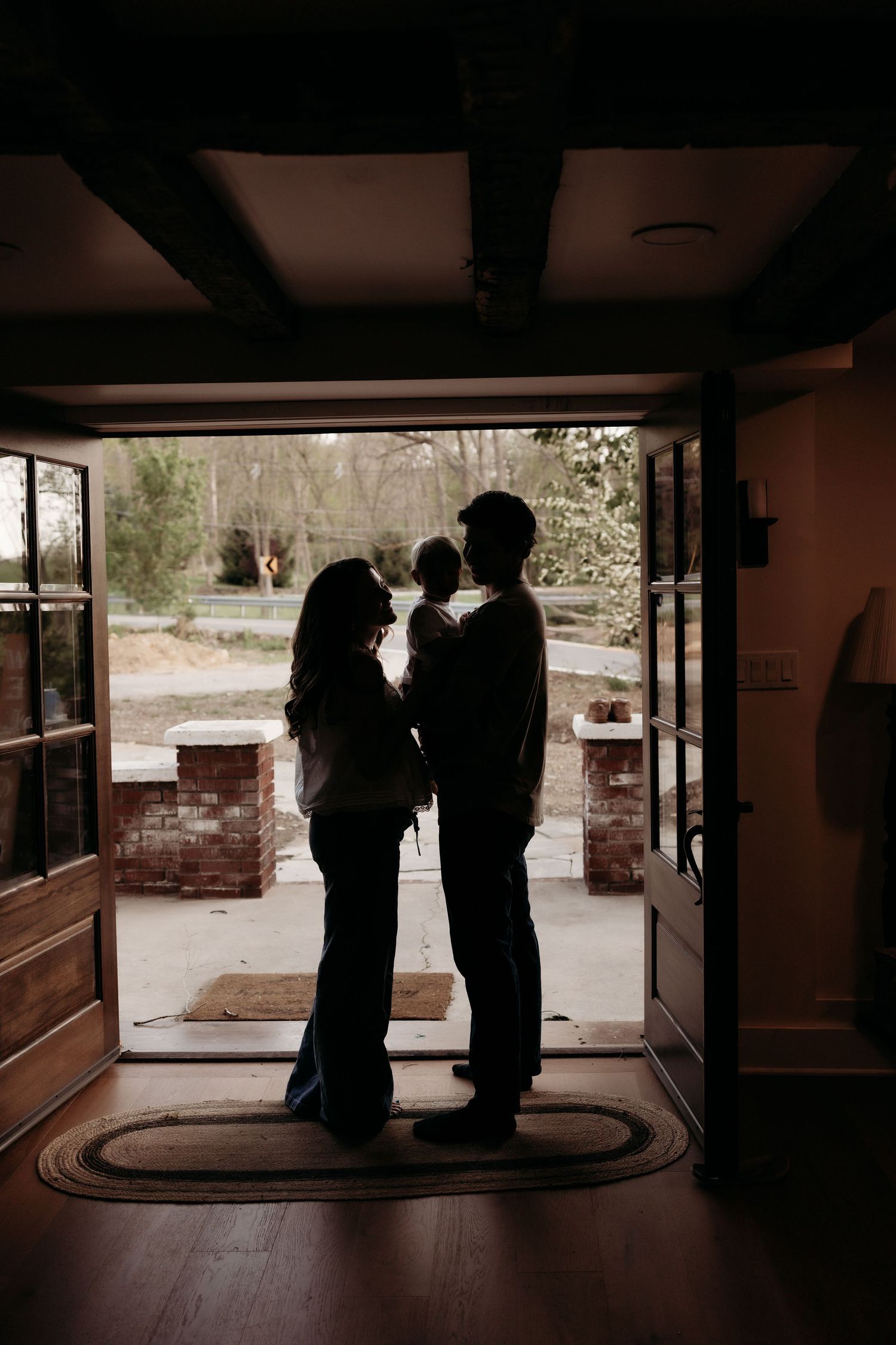 Silhouette of couple holding baby standing in open doorway with outdoor light.