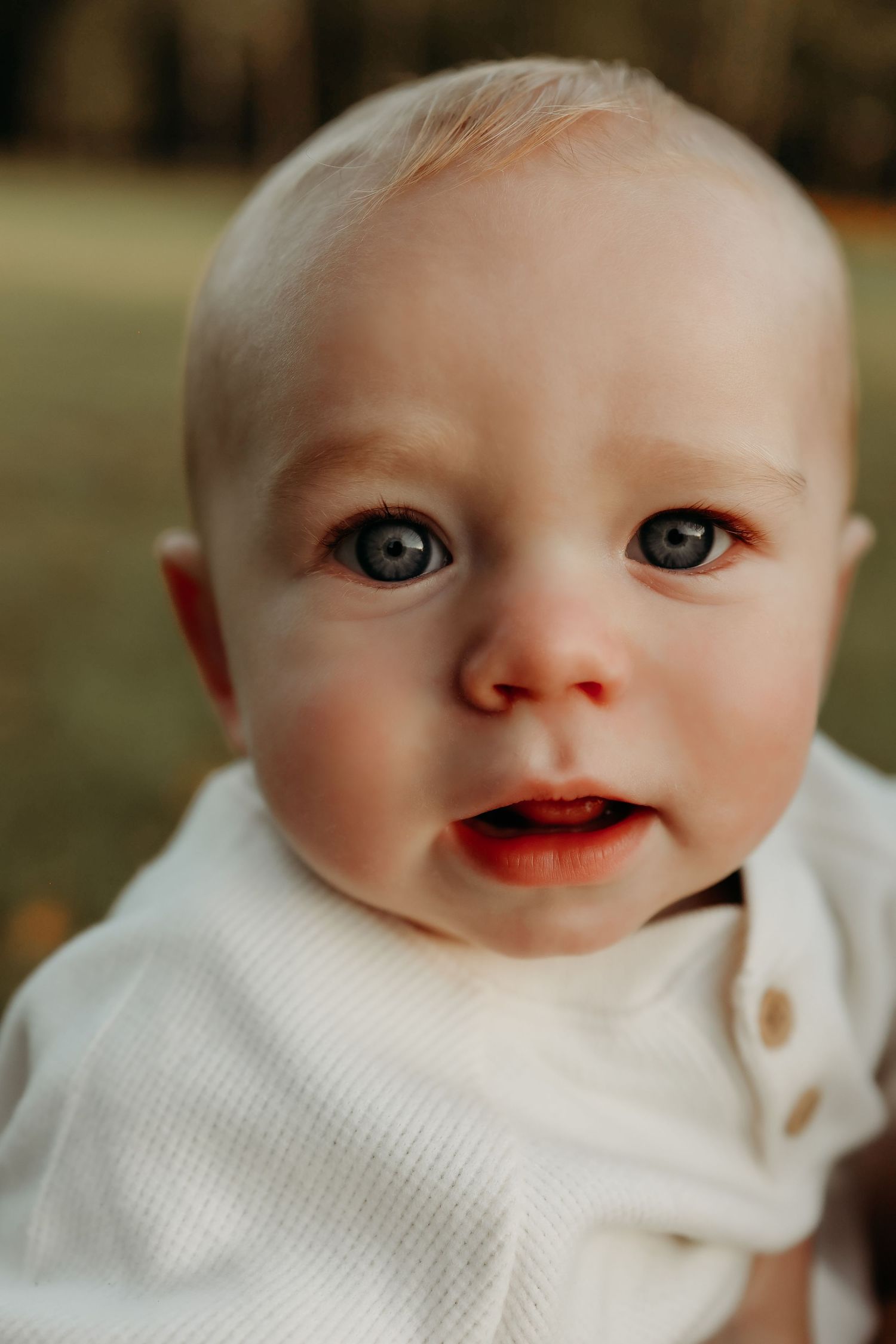 Close-up portrait of adorable blue-eyed baby with light hair in white outfit.