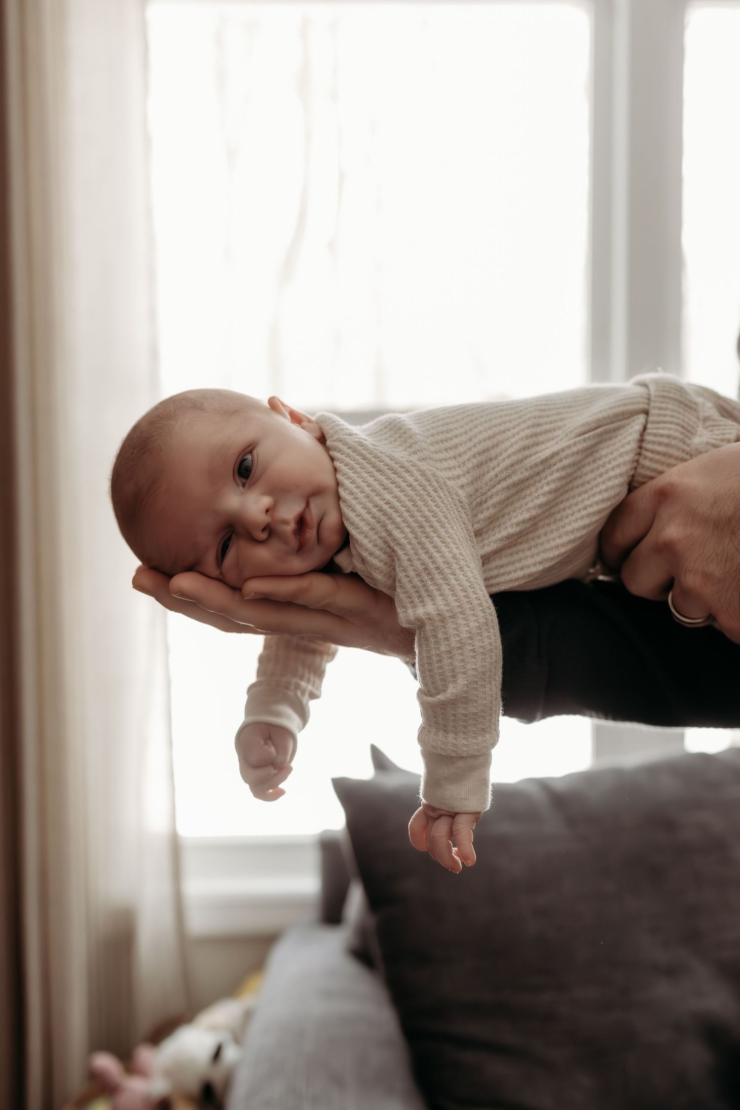 A sequence of photos showing a baby in a beige sweater rolling over on a dark couch near a window.